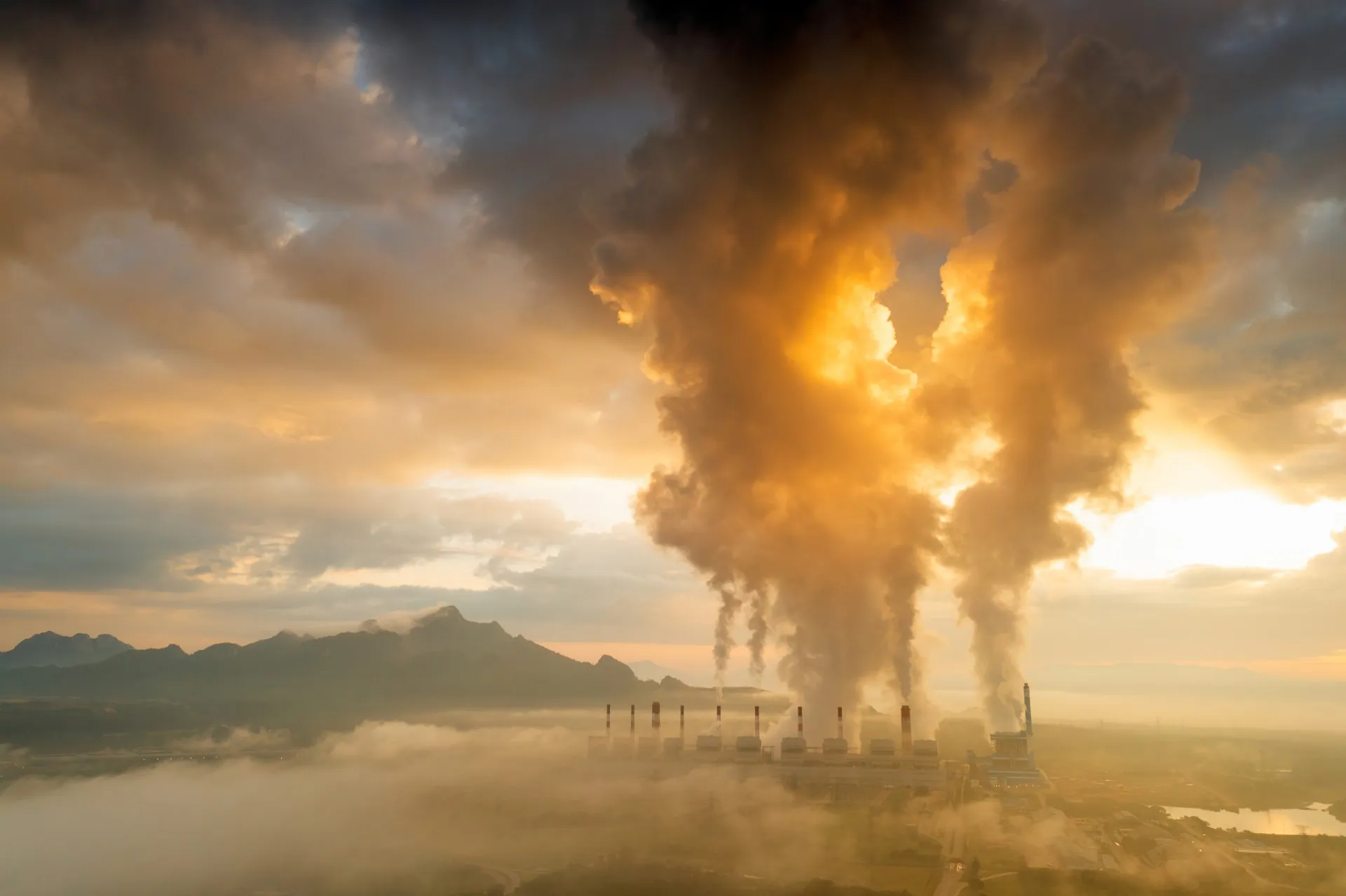 Usina de energia a carvão com grandes chaminés liberando fumaça no céu.
