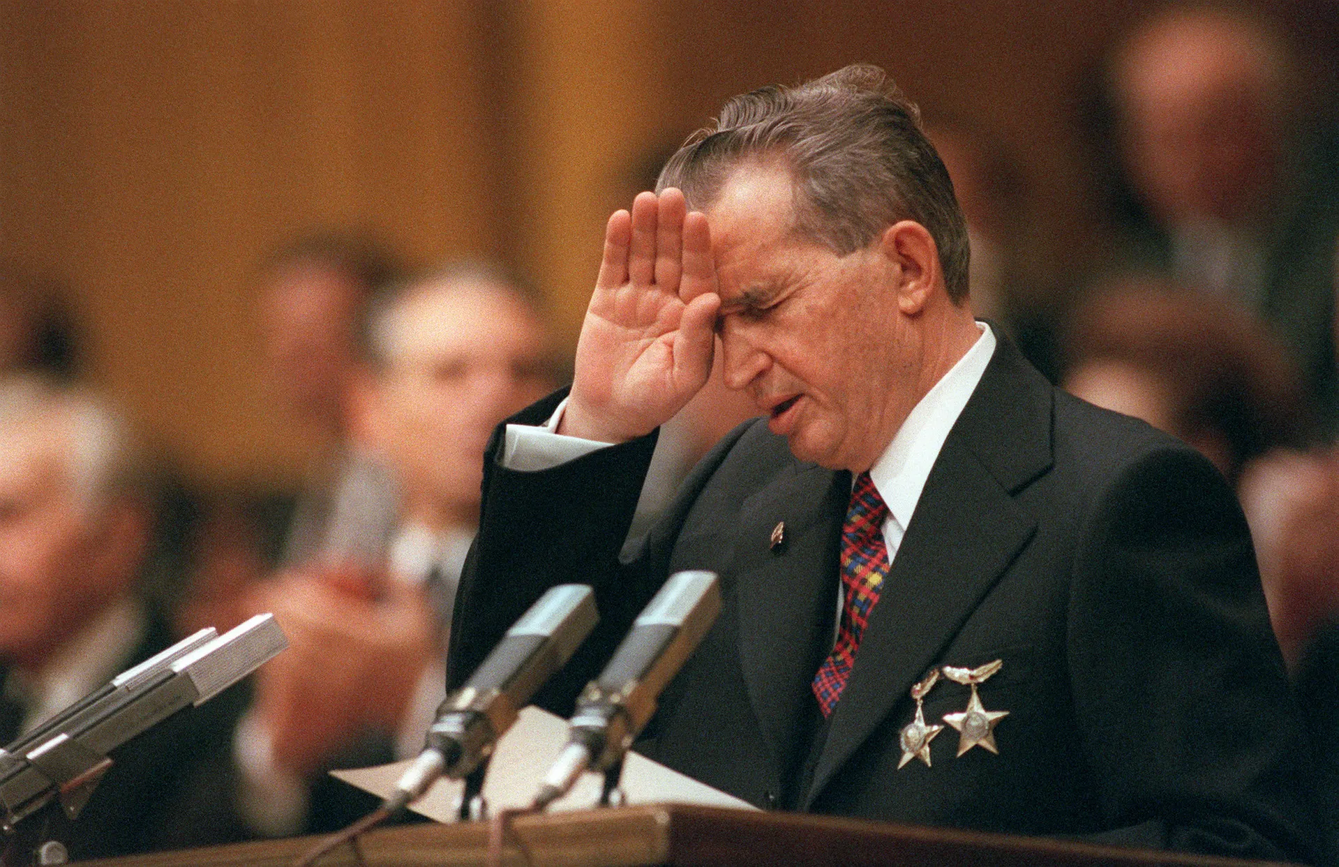 Nicolae Ceaușescu, ditador romeno, acenando durante um evento oficial, com expressão severa.