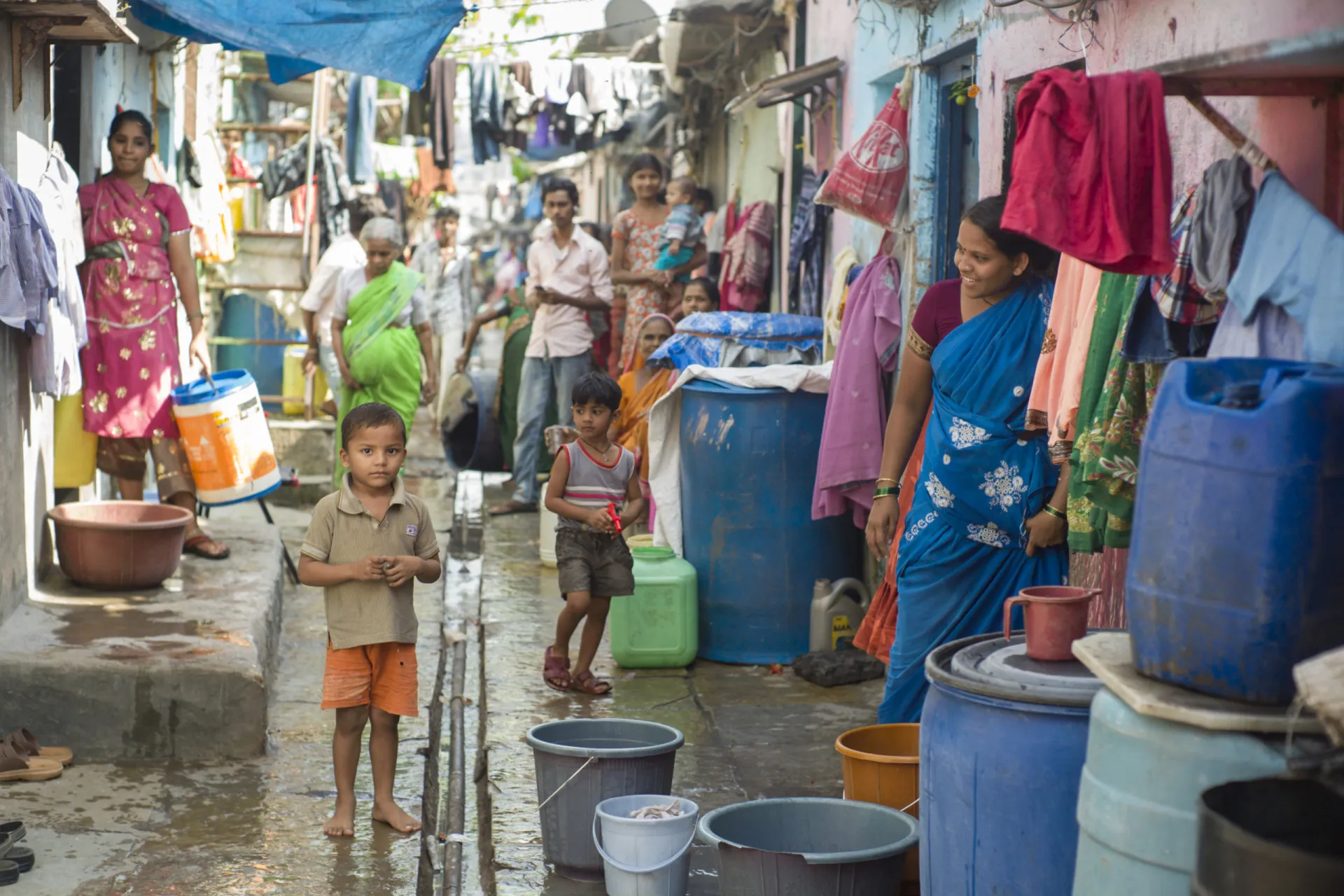 Uma rua estreita e movimentada dentro da favela de Dharavi, com pessoas e mercadorias.