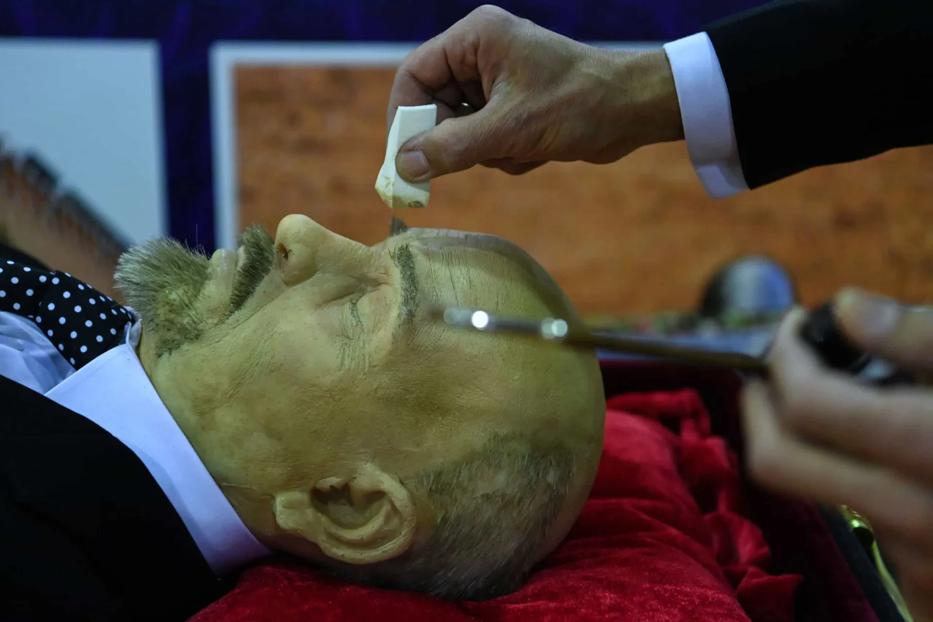 Corpo de um santo exposto em uma urna de vidro, coberto por cera para preservação.