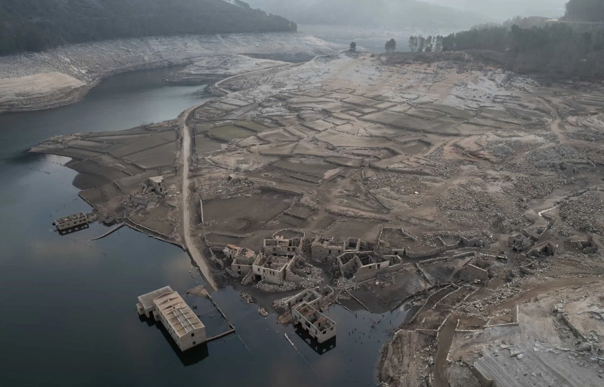 Ruínas da vila de Aceredo, com paredes de pedra e telhados desabados, no leito seco de um reservatório.