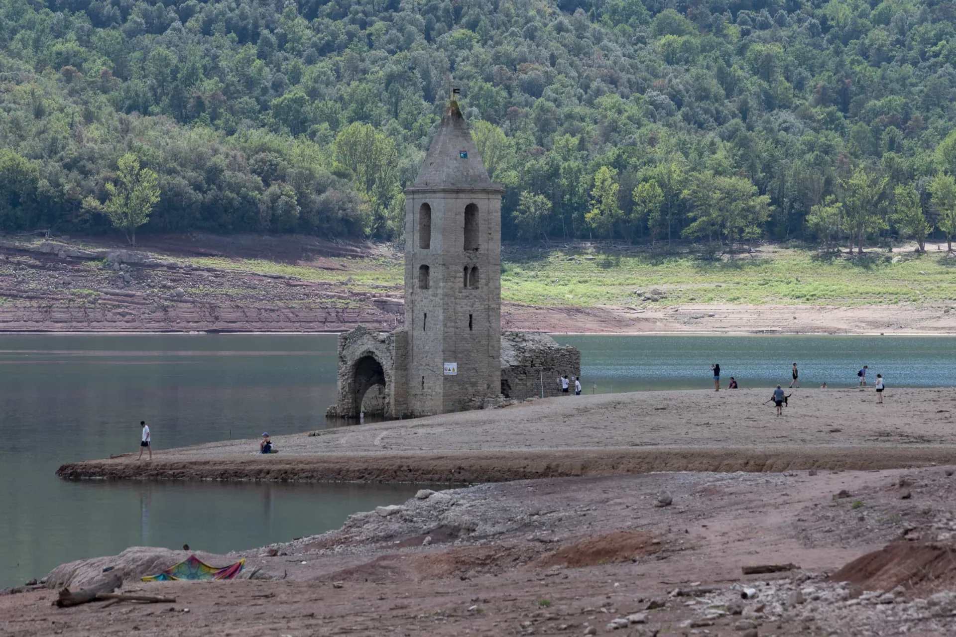 A Igreja de Sant Romà completamente exposta no leito seco do reservatório, com pessoas caminhando ao redor.