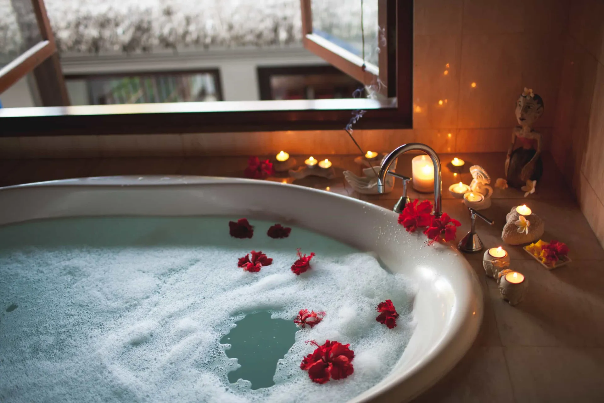 Pés de uma pessoa relaxando em uma banheira com espuma e pétalas de flores.
