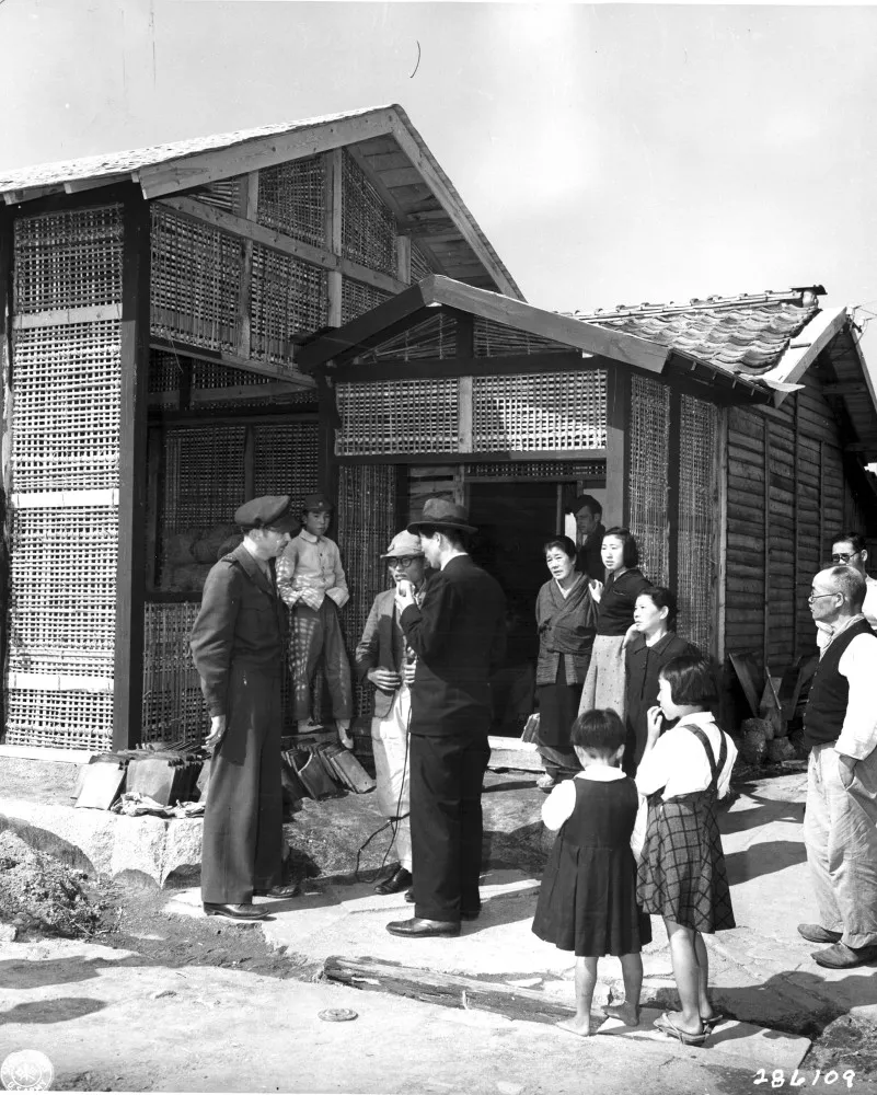 Um detetive particular japonês da era de 1940, em seu escritório, olhando papéis em uma mesa.