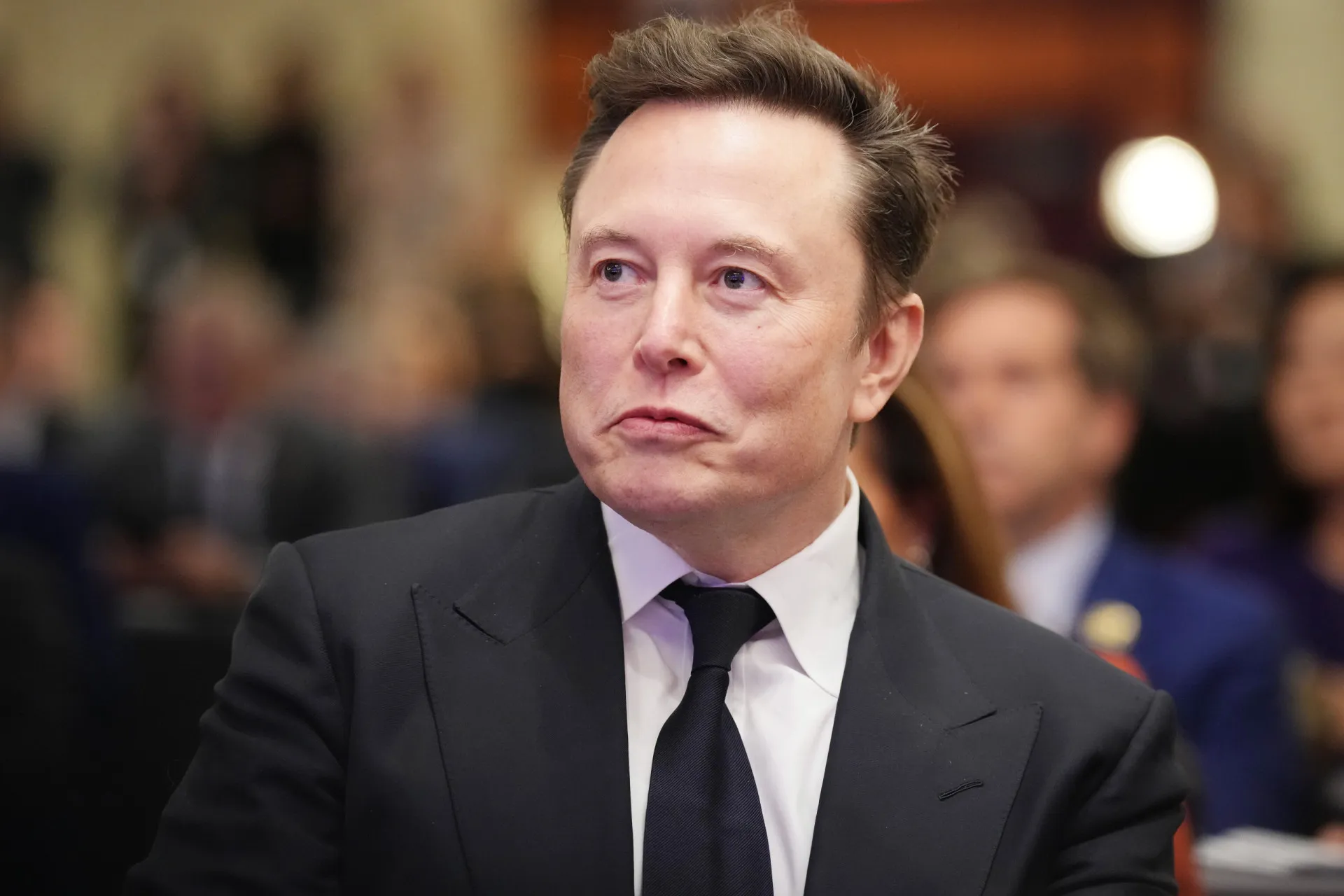 Elon Musk em um evento, gesticulando enquanto fala, com uma expressão intensa.