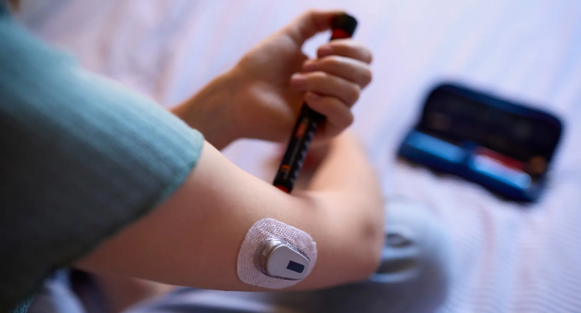 Medidor de glicose mostrando um nível baixo de açúcar no sangue, com uma pessoa dormindo ao fundo.