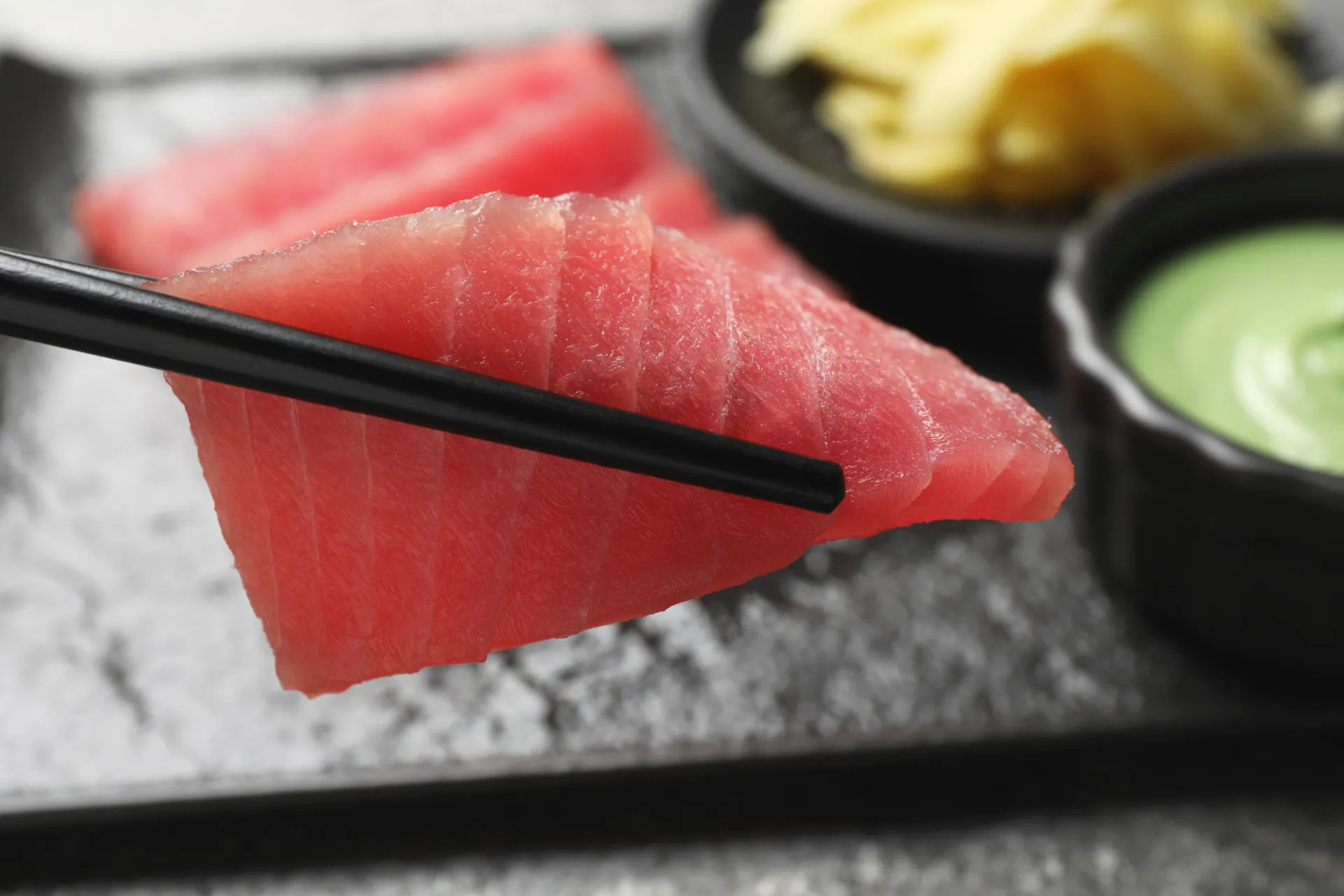 Uma mão segurando hashis para pegar um pedaço de sushi, simbolizando o consumo.