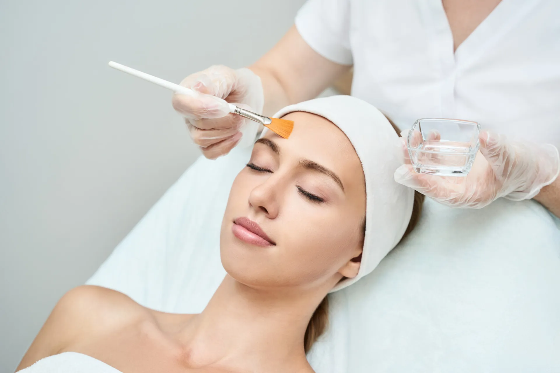 Profissional aplicando uma solução de peeling químico no rosto de uma cliente.