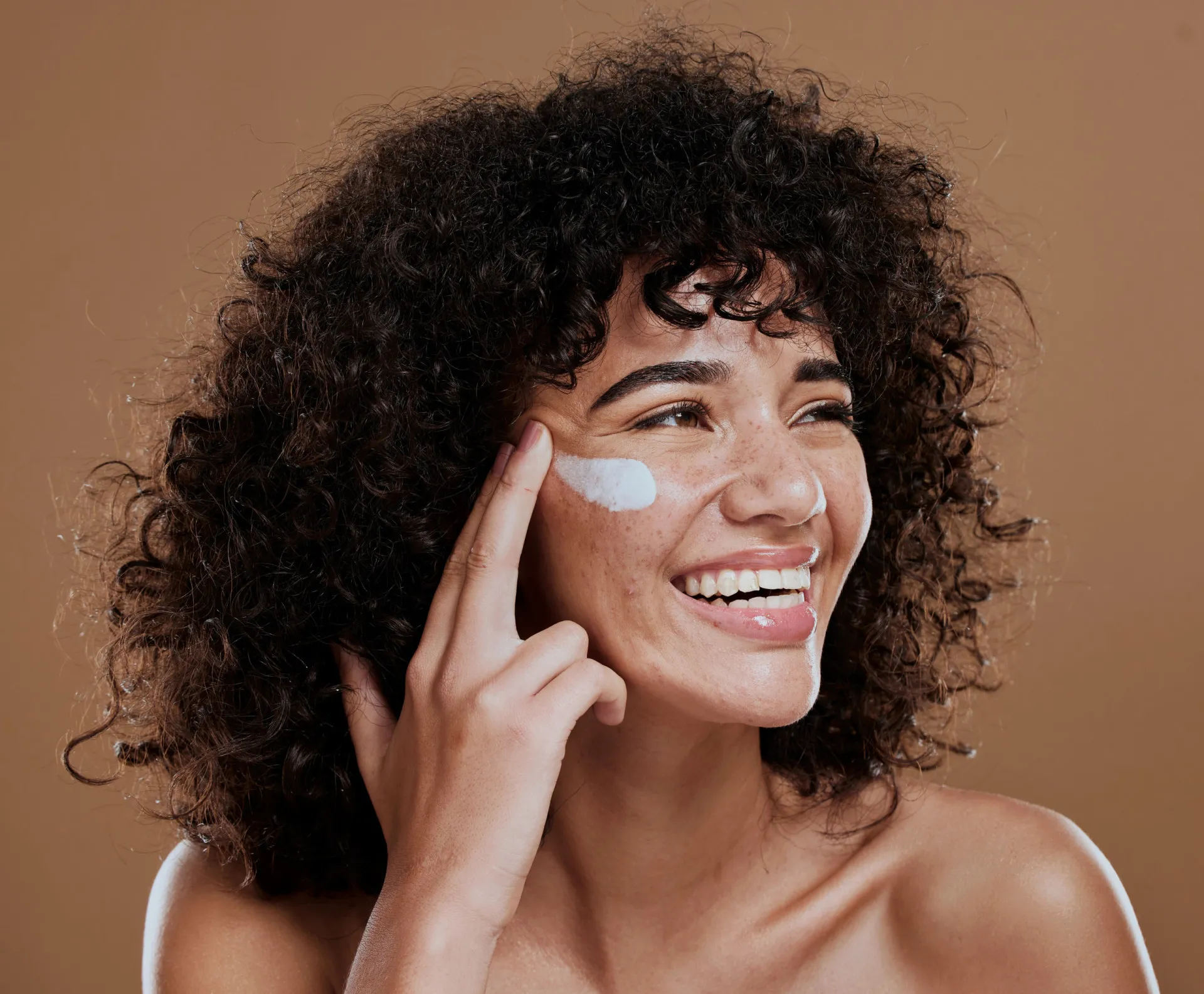 Mão aplicando um creme antirrugas no rosto, demonstrando a aplicação de produtos de skincare.