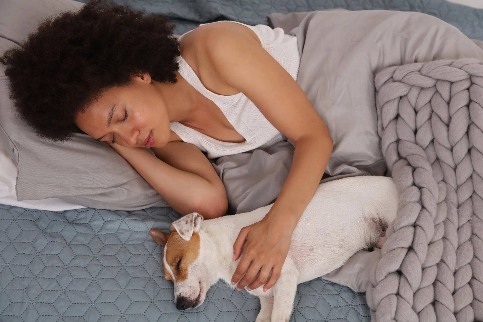 Mulher deitada na cama com seu cachorro e seu gato, olhando para a câmera.