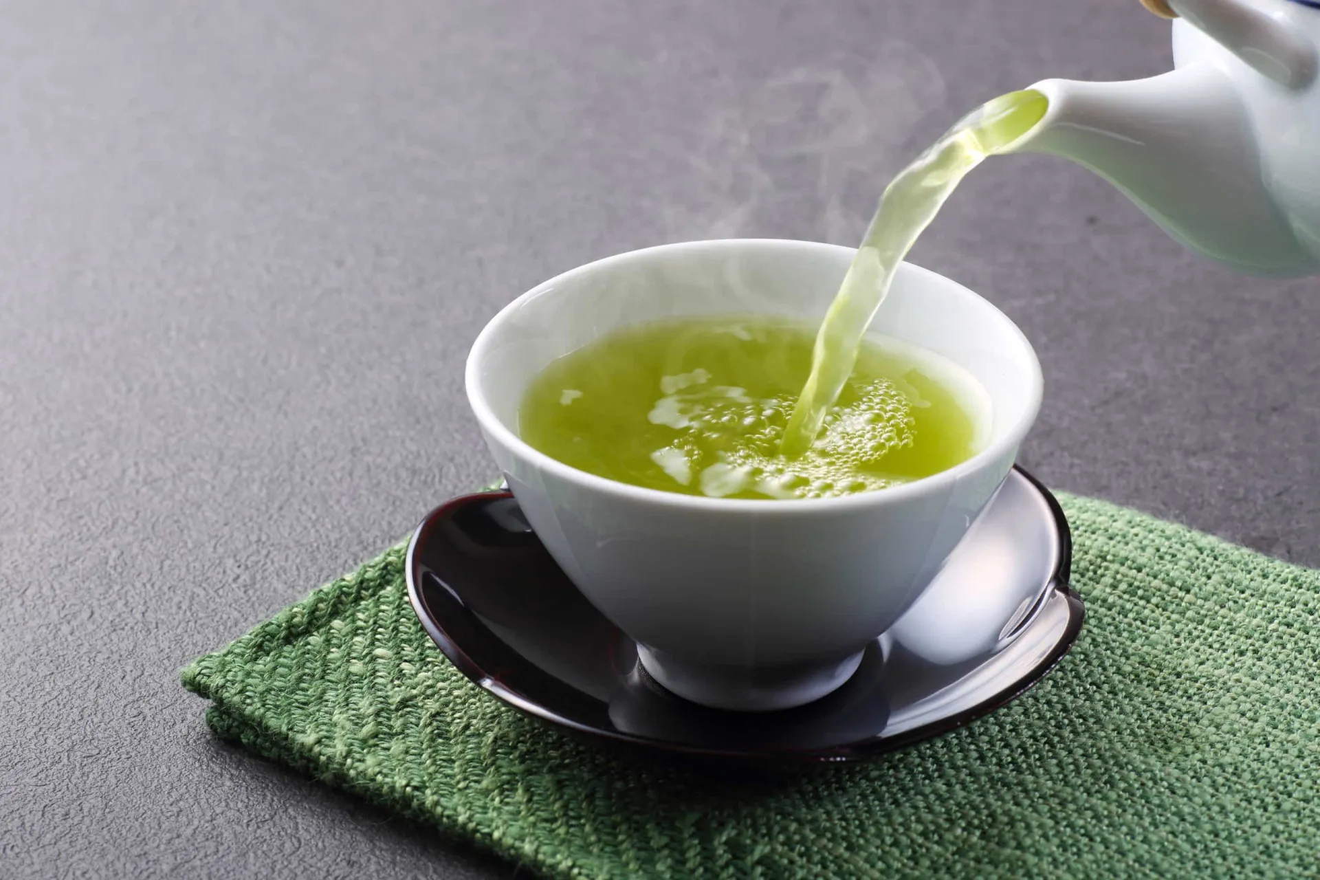 Xícara de chá verde fumegante, com folhas de chá ao lado.