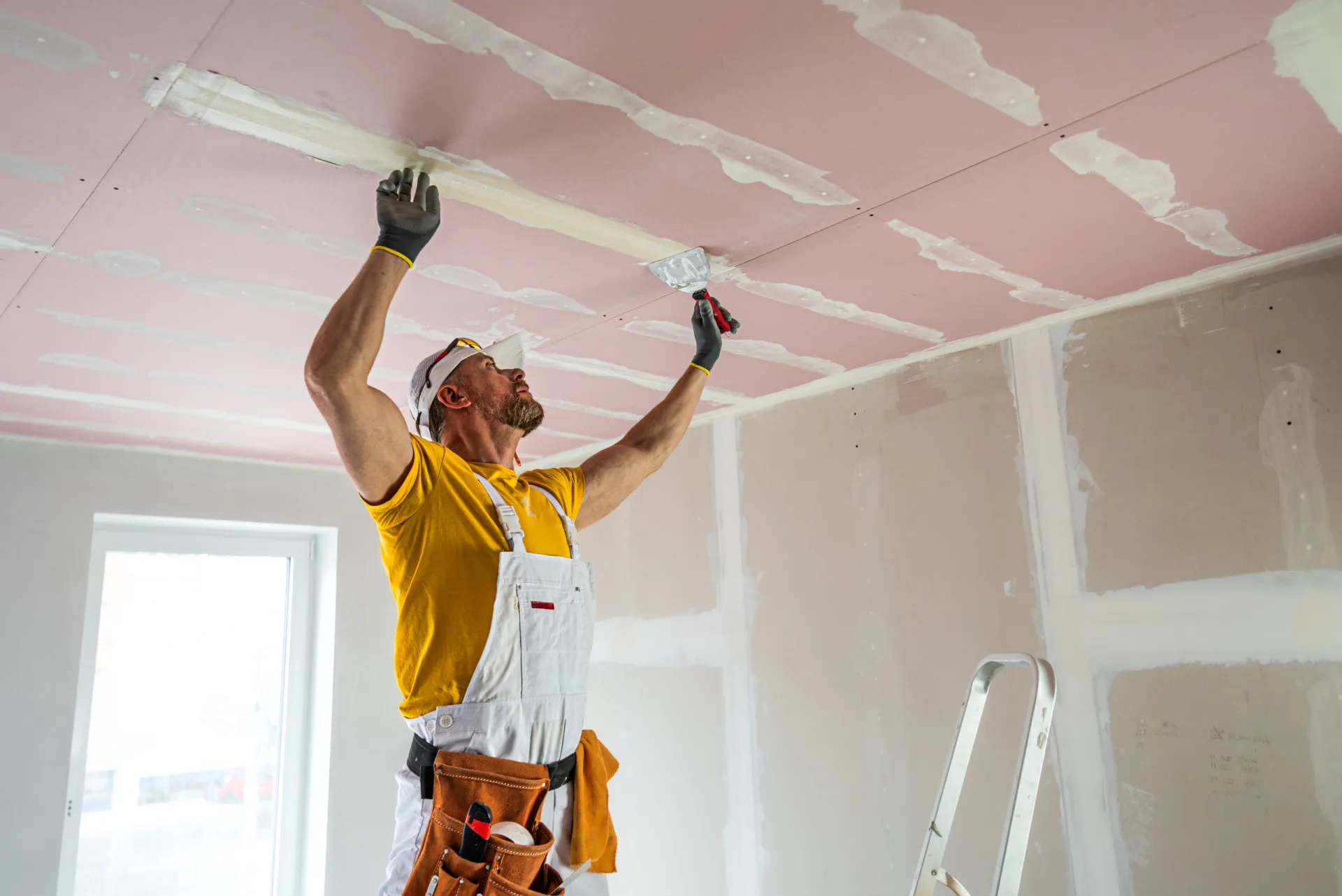 Homem pintando uma parede de branco com um rolo de pintura.