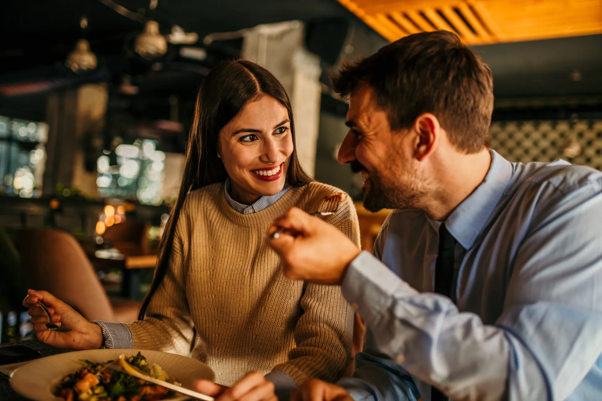 Casal sorrindo e brindando com taças de vinho em um restaurante.