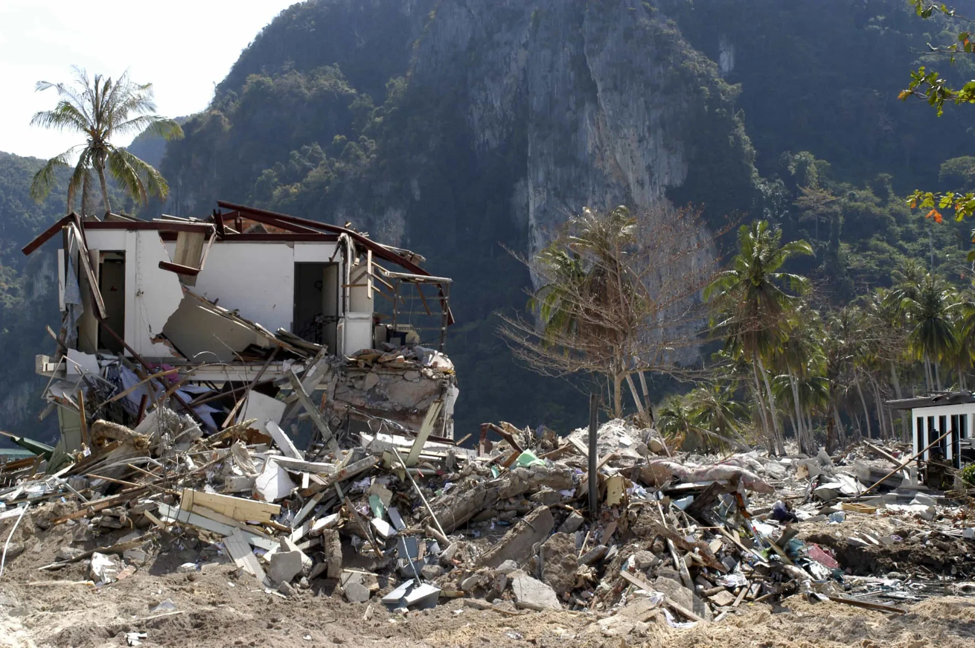 Pessoas desabrigadas em meio aos escombros após o tsunami, com expressões de choque e tristeza.