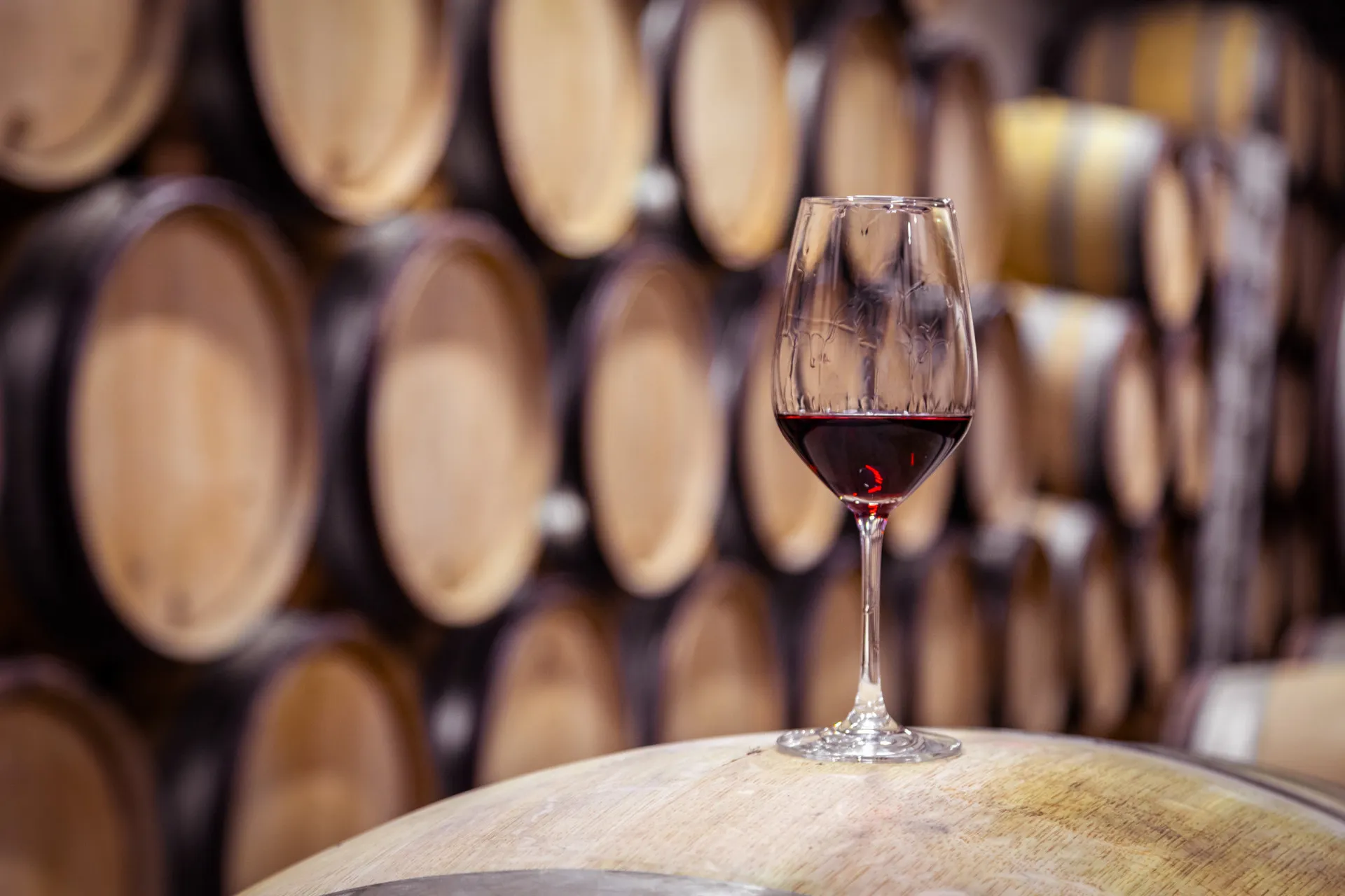 Uma taça de vinho tinto ao lado de uma garrafa e uvas em um barril de madeira.