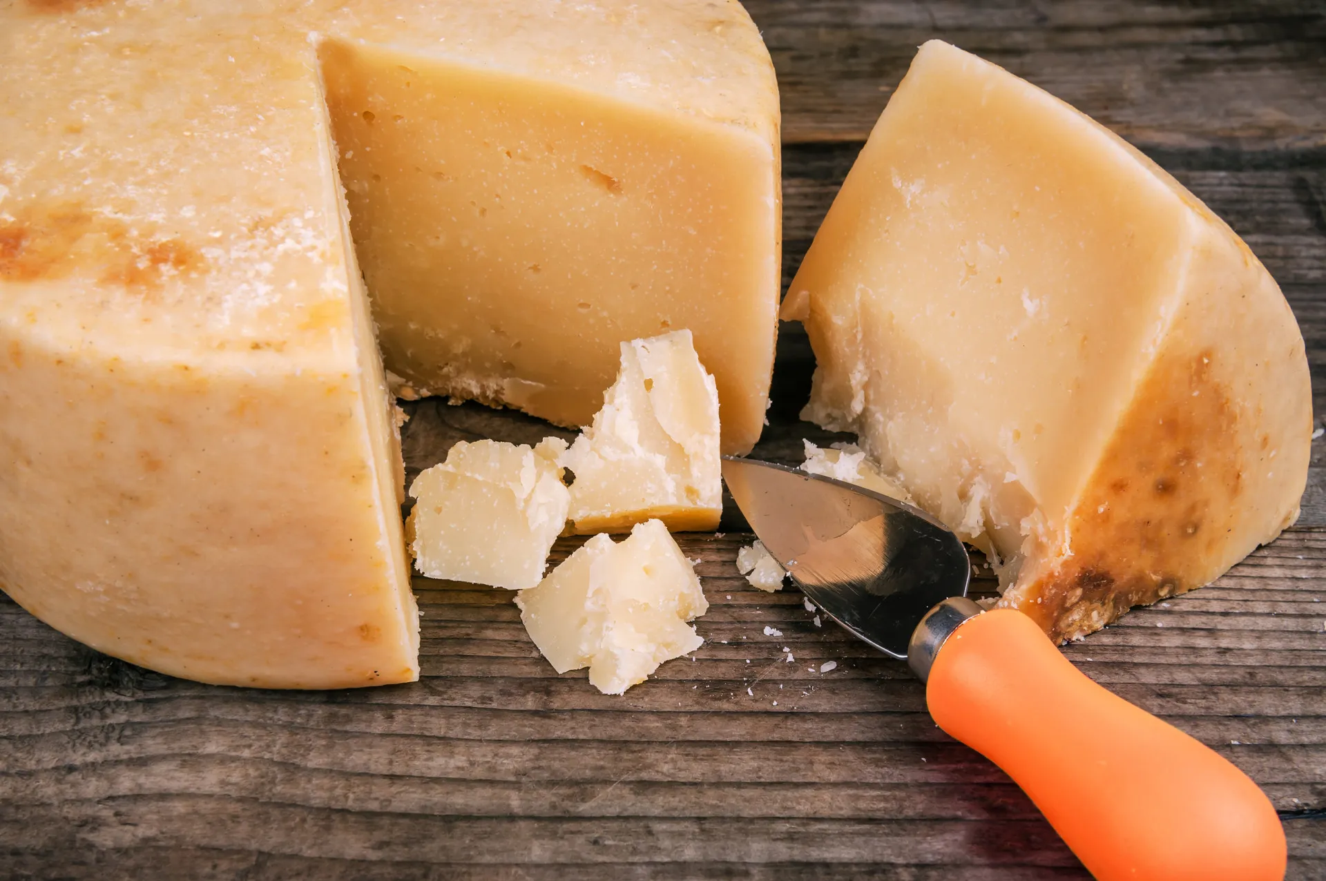 Vários tipos de queijos curados, como parmesão e manchego, dispostos em uma tábua de madeira.