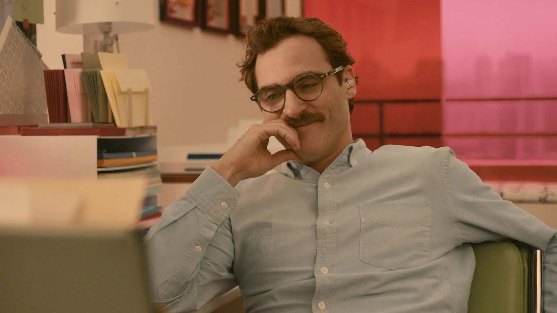 Joaquin Phoenix como Theodore, olhando com ternura enquanto conversa com seu sistema operacional.