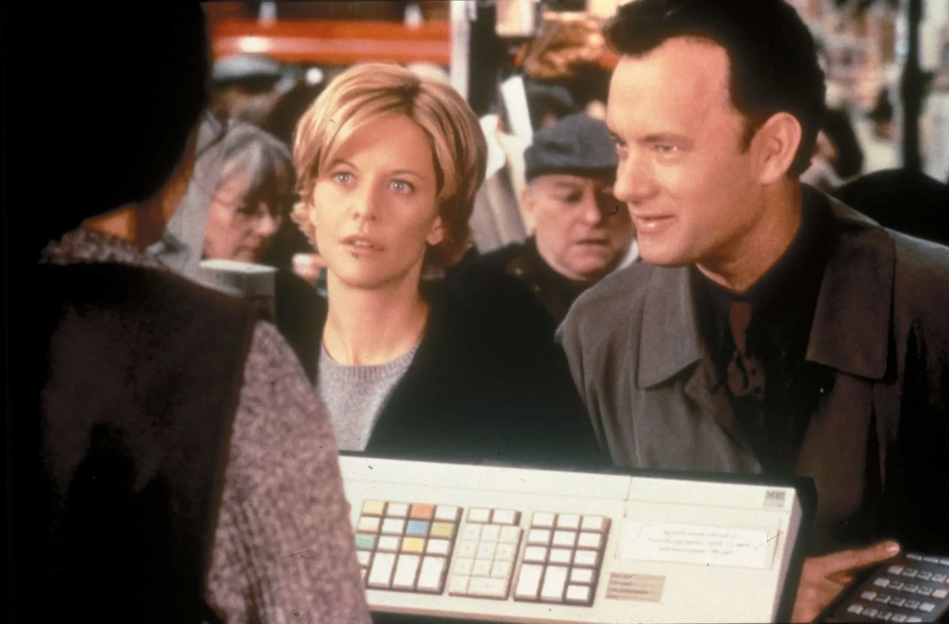 Tom Hanks e Meg Ryan sorrindo um para o outro em uma cena da comédia romântica 'Mensagem Para Você'.
