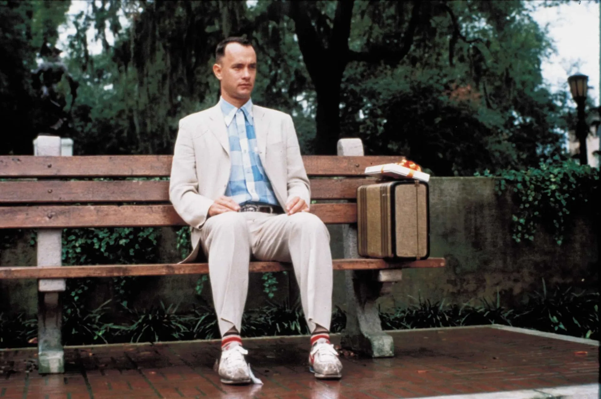 Tom Hanks como Forrest Gump, sentado em um banco com sua caixa de bombons.
