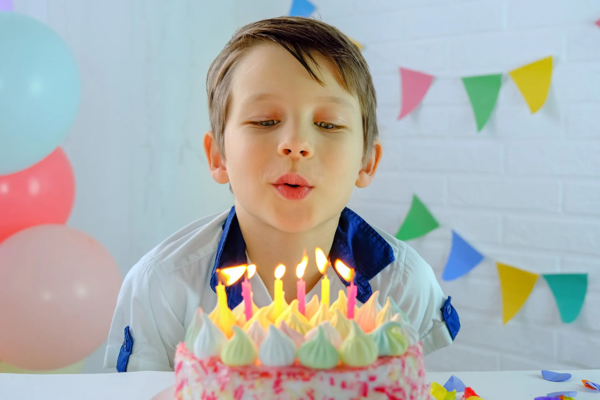 Crianças sorrindo ao redor de um bolo de aniversário com velas acesas, prestes a soprar.
