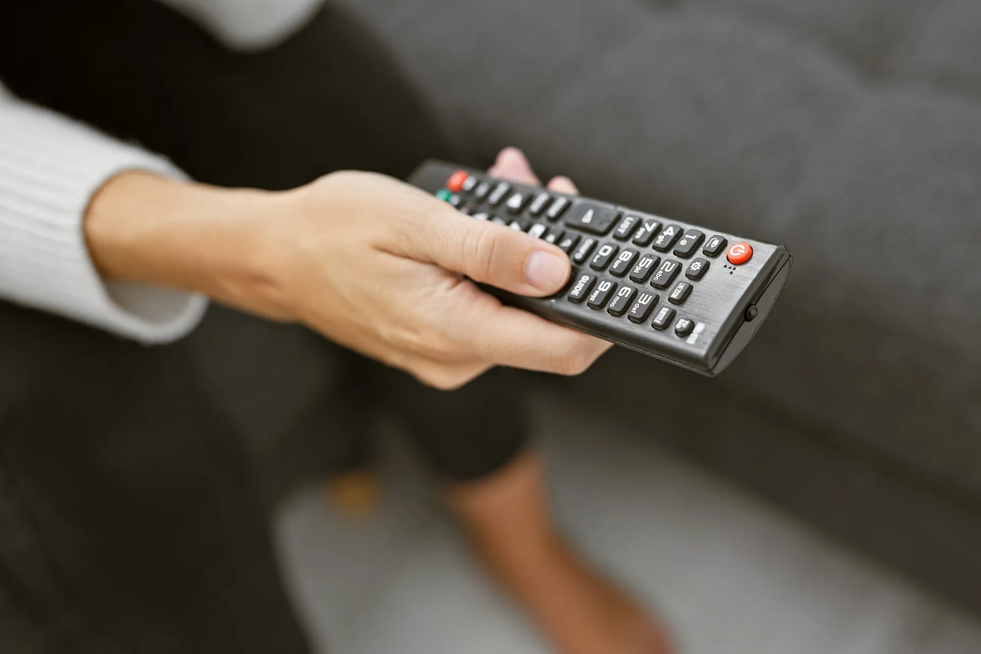 Uma pessoa segurando um controle remoto de TV, objeto que passa por muitas mãos.