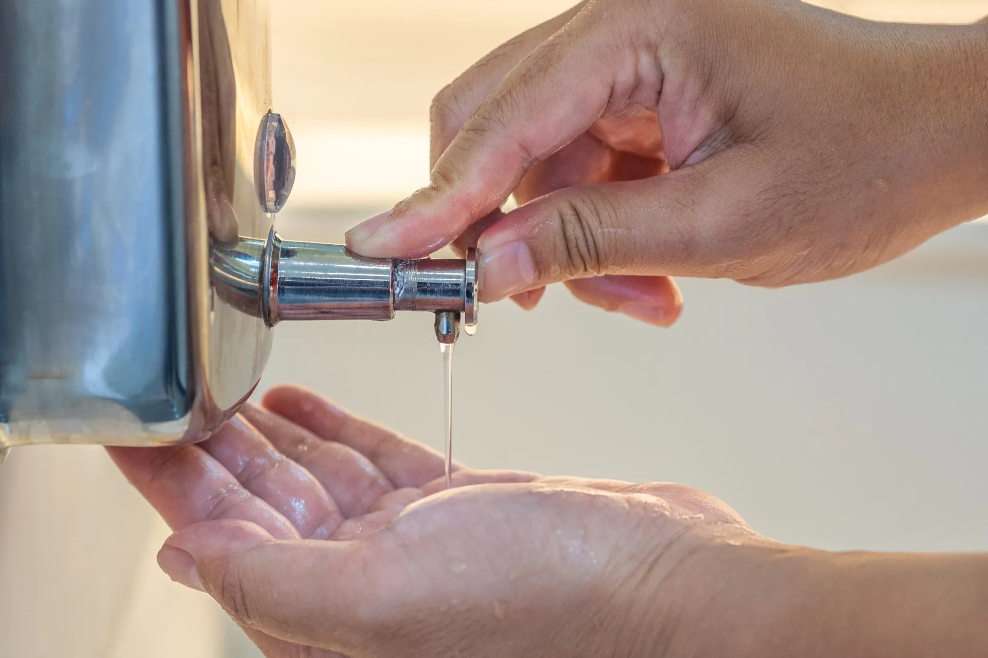 Uma mão pressionando um dispensador de sabão líquido em um banheiro público.