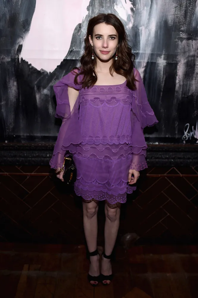 Emma Roberts tentando segurar uma manga de seu vestido que se soltou.