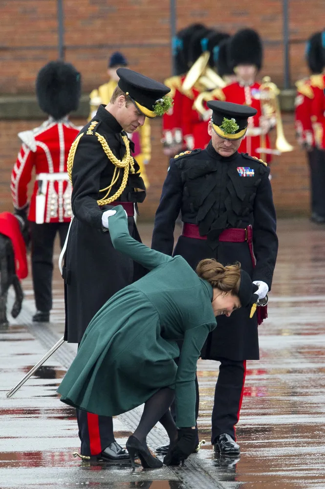 Kate Middleton com o salto de seu sapato preso em uma grade no chão durante um evento.