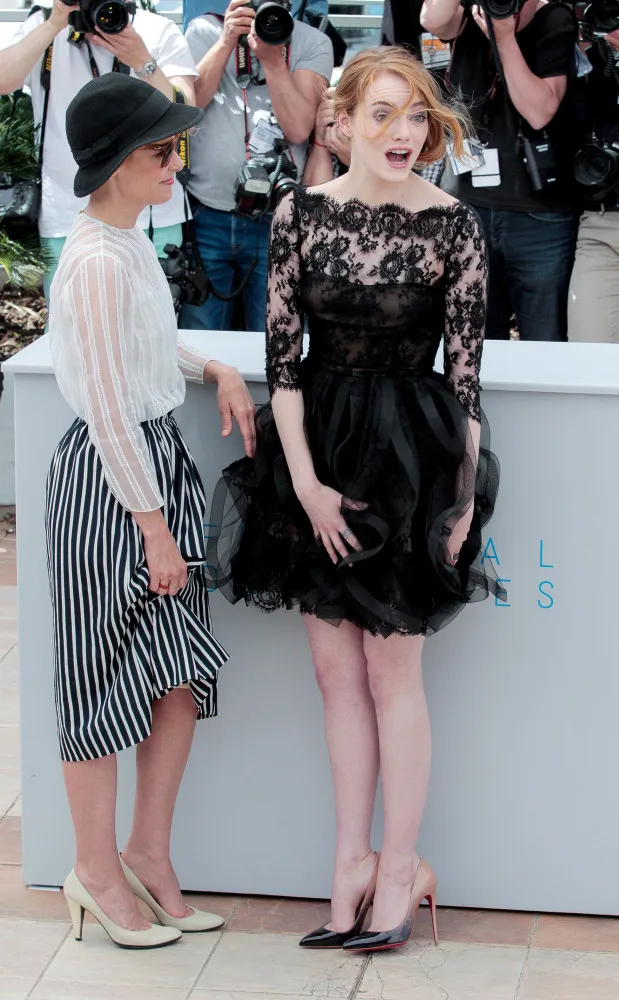 Emma Stone rindo enquanto tenta segurar sua saia curta que foi levantada por uma forte rajada de vento.