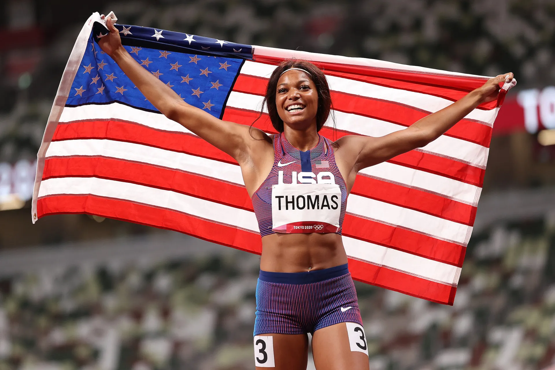 A velocista americana Gabby Thomas sorrindo e acenando para o público.