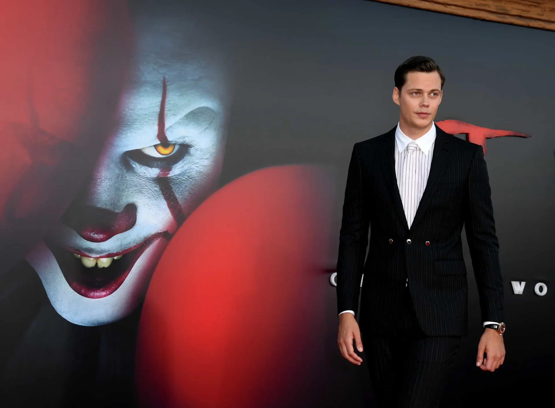 O ator Bill Skarsgård sorrindo de forma charmosa em um evento, contrastando com seu papel de Pennywise.