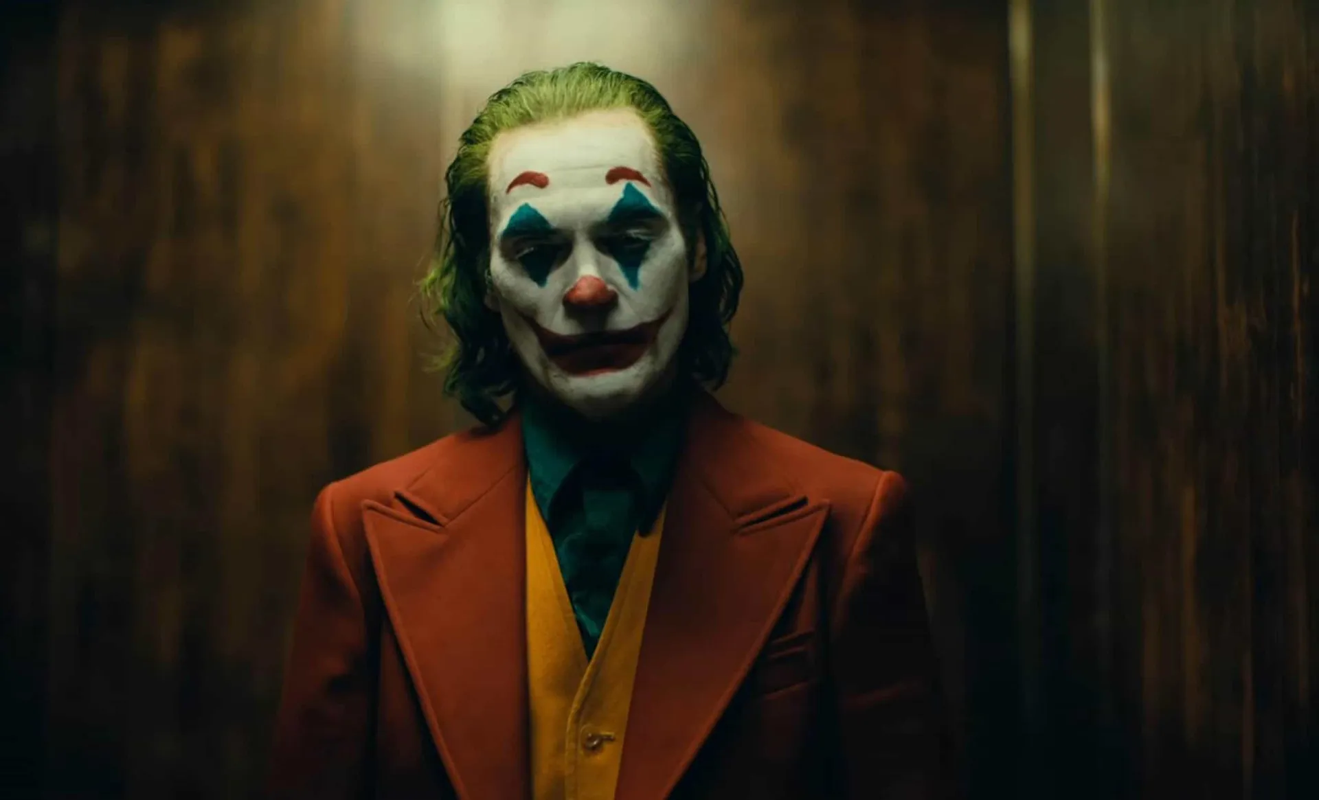 Joaquin Phoenix como o Coringa, com maquiagem de palhaço e um olhar perturbado e melancólico.