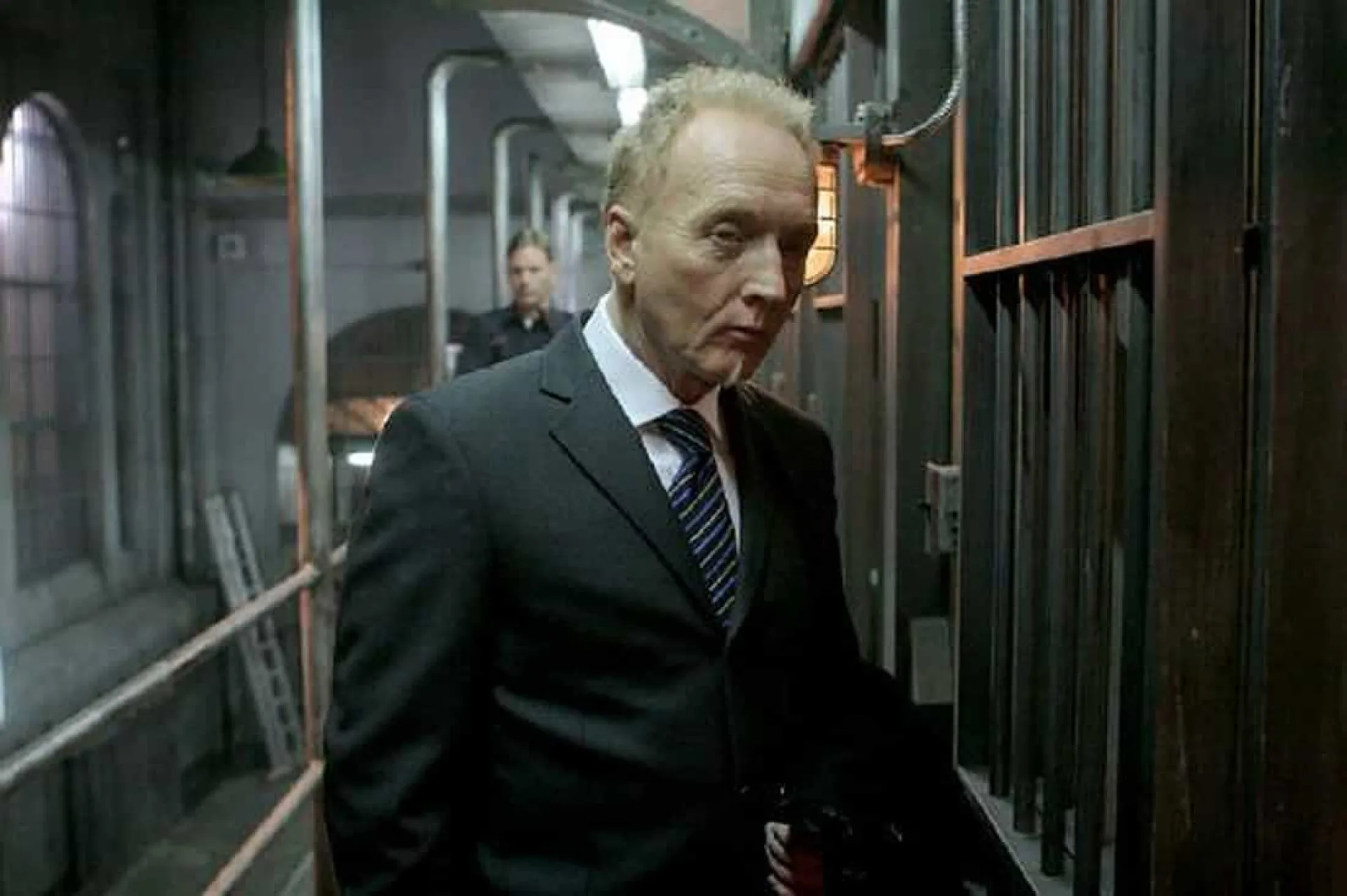Tobin Bell com uma expressão séria e calculista, lembrando seu personagem Jigsaw da franquia 'Jogos Mortais'.