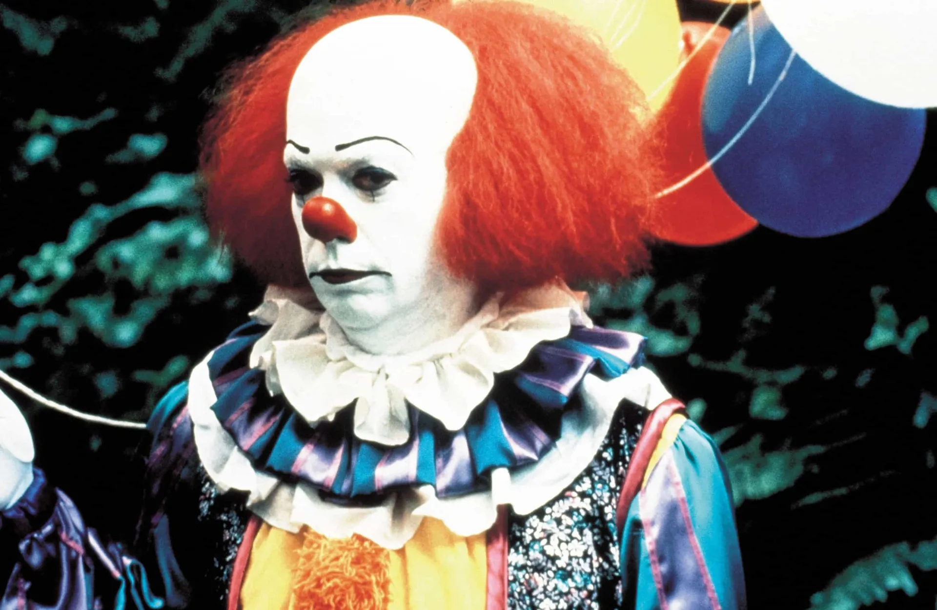 Tim Curry como o palhaço Pennywise na minissérie 'It', com um sorriso aterrorizante.