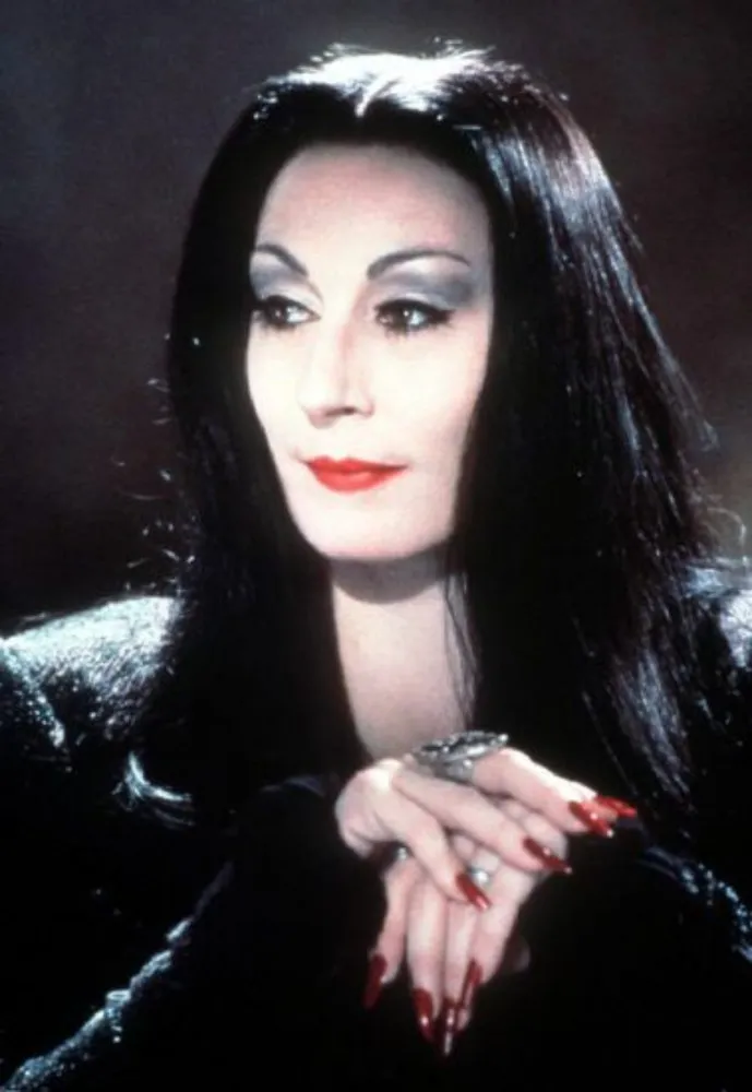 Anjelica Huston como Morticia Addams, com um vestido preto justo e olhar enigmático.
