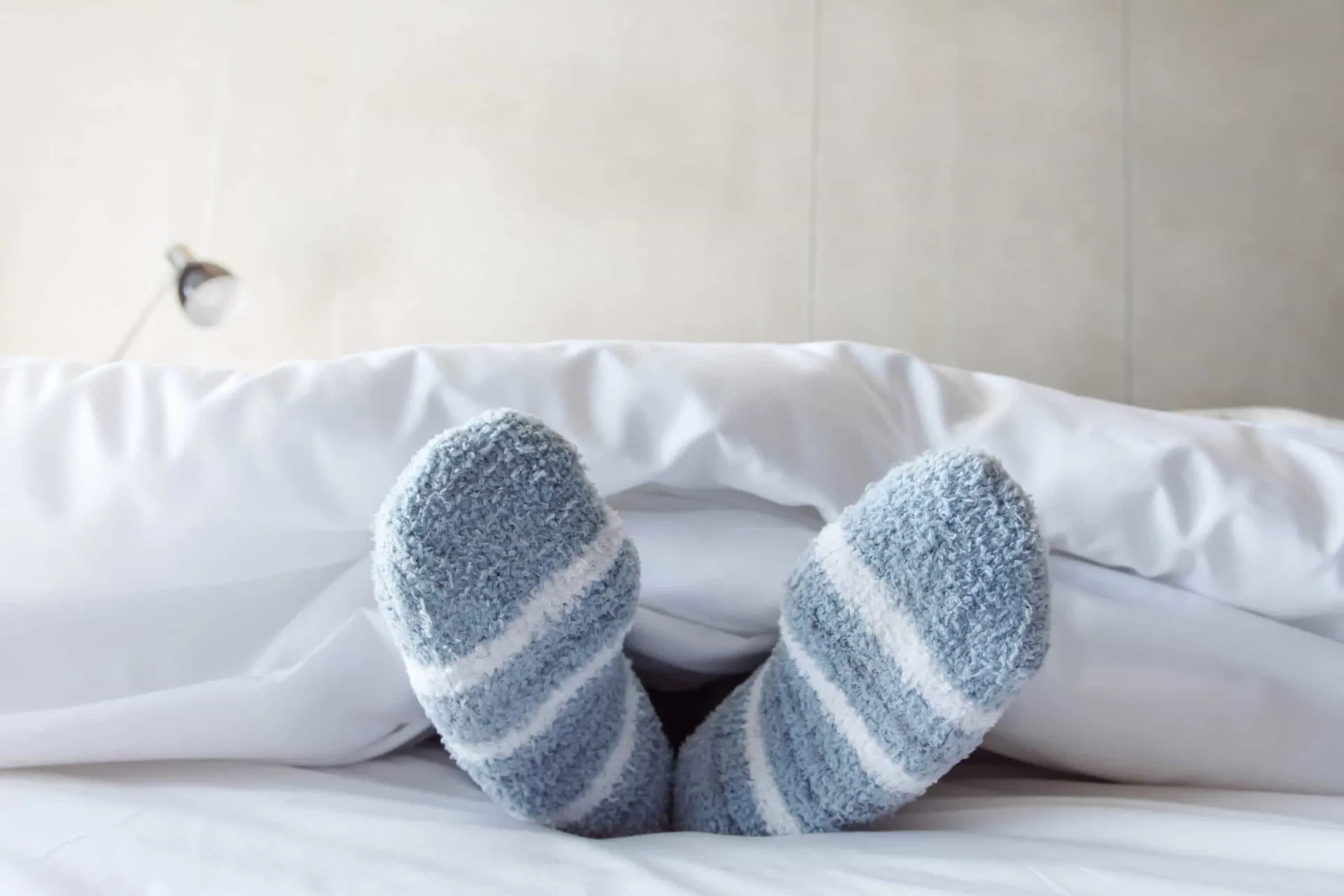 Pés de uma pessoa na cama, usando meias de lã grossas e quentes para se proteger do frio durante a noite.