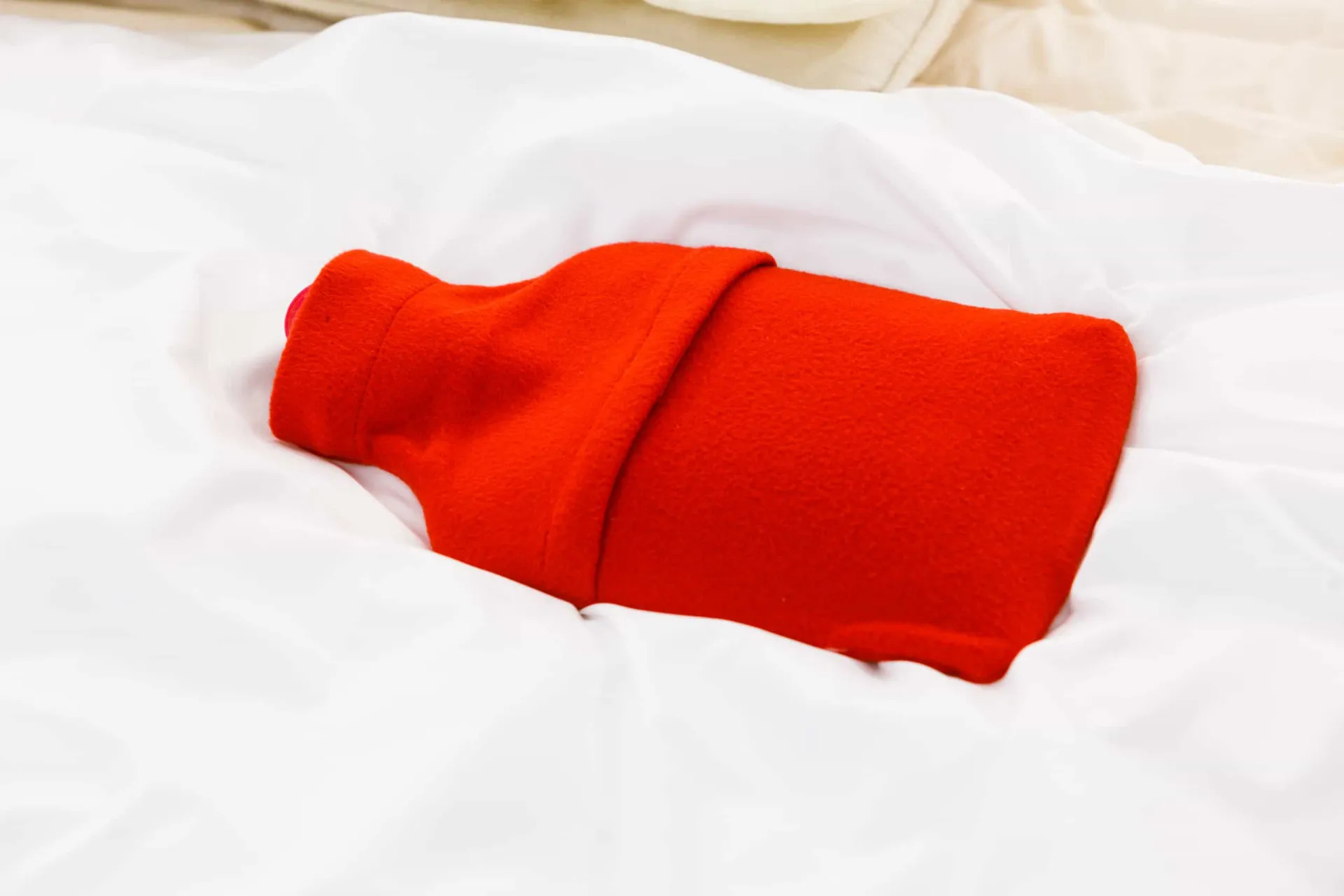 Uma bolsa de água quente vermelha posicionada sobre uma cama com lençóis brancos, aquecendo o local.