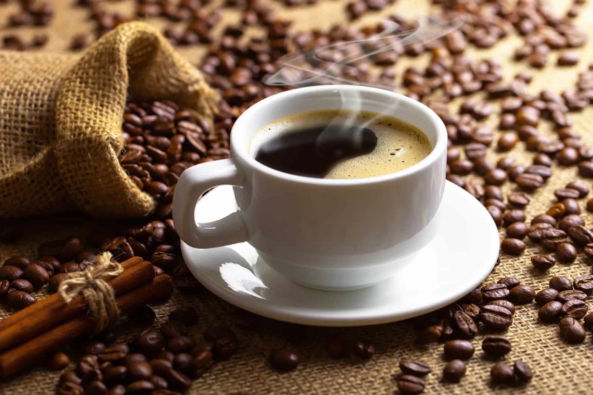 Uma xícara de café preto forte com grãos de café espalhados ao redor.
