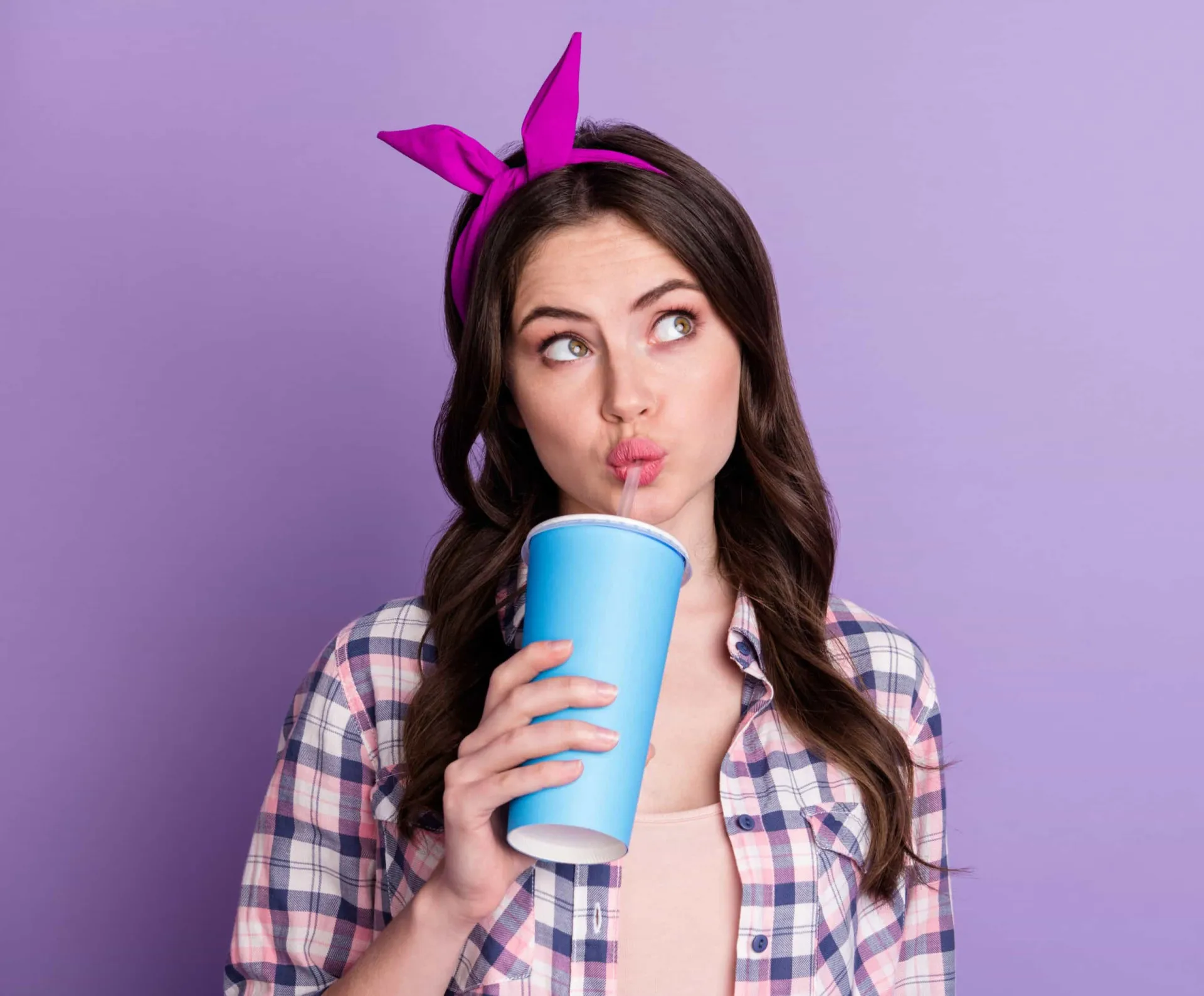 Uma mulher bebendo um suco escuro com um canudo, minimizando o contato com os dentes.
