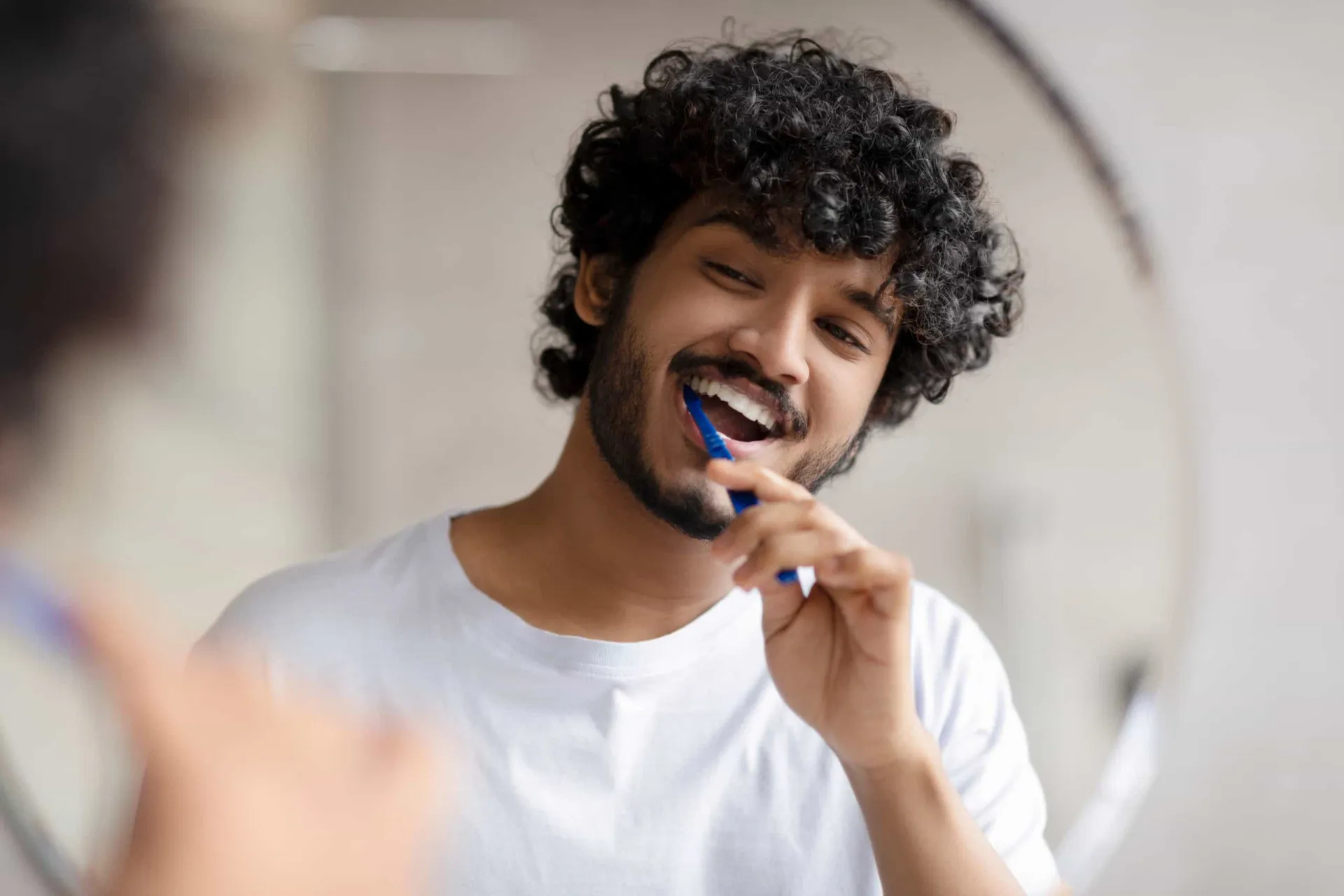 Uma pessoa escovando os dentes com atenção em frente a um espelho de banheiro.