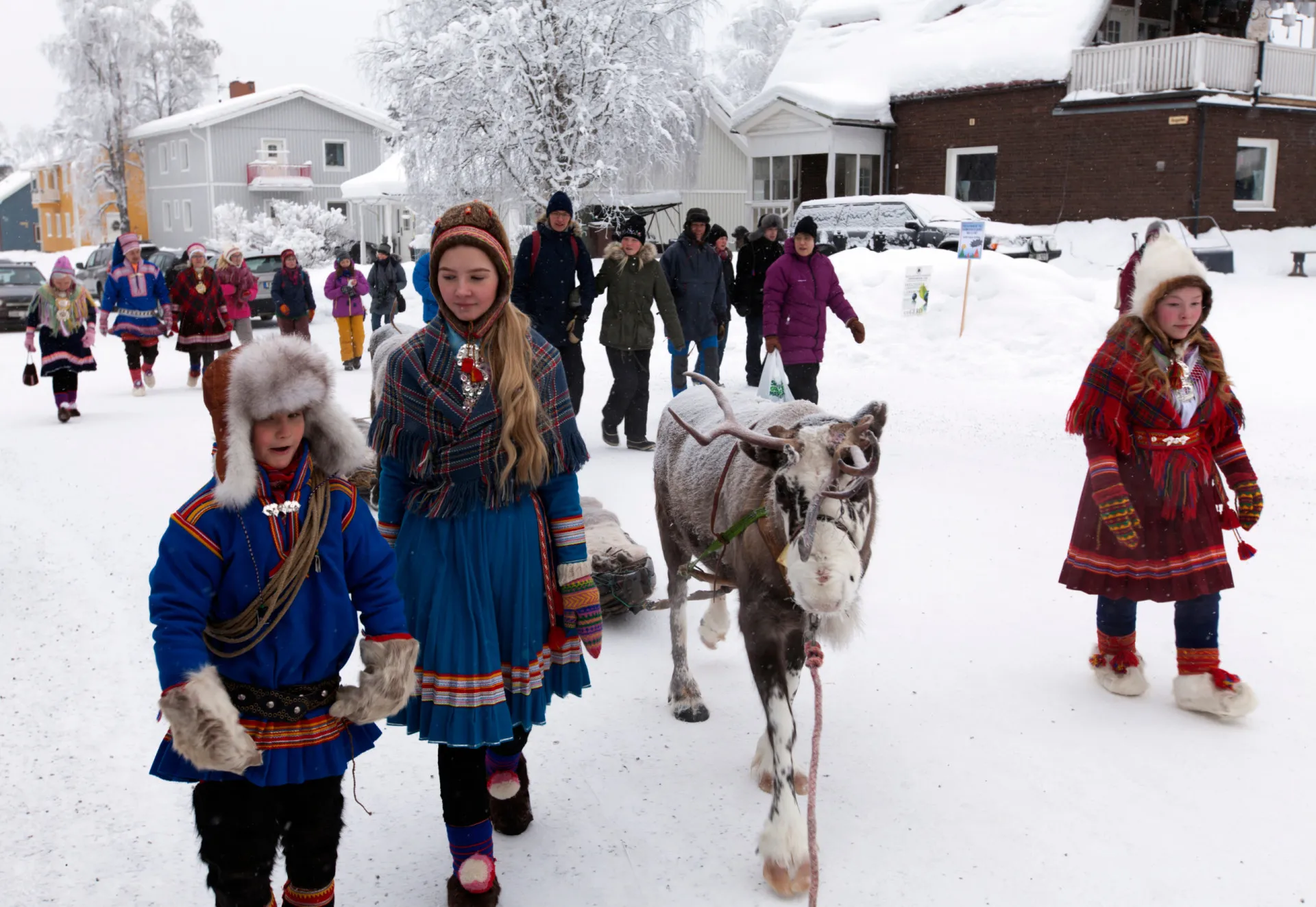 Uma pessoa do povo Sámi em traje tradicional colorido, ao lado de uma rena.