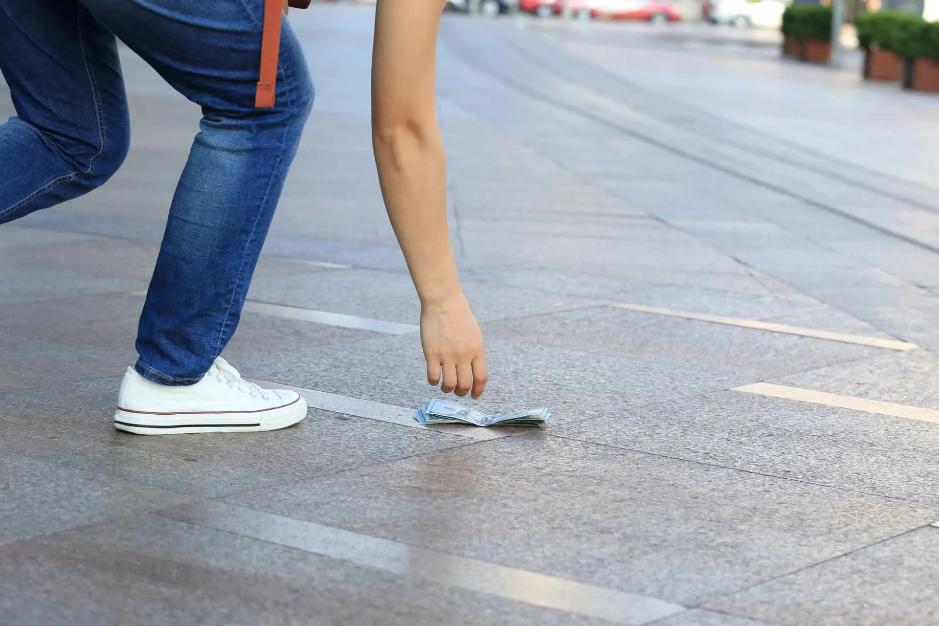 Uma nota de dinheiro caída no chão de paralelepípedos de uma rua.