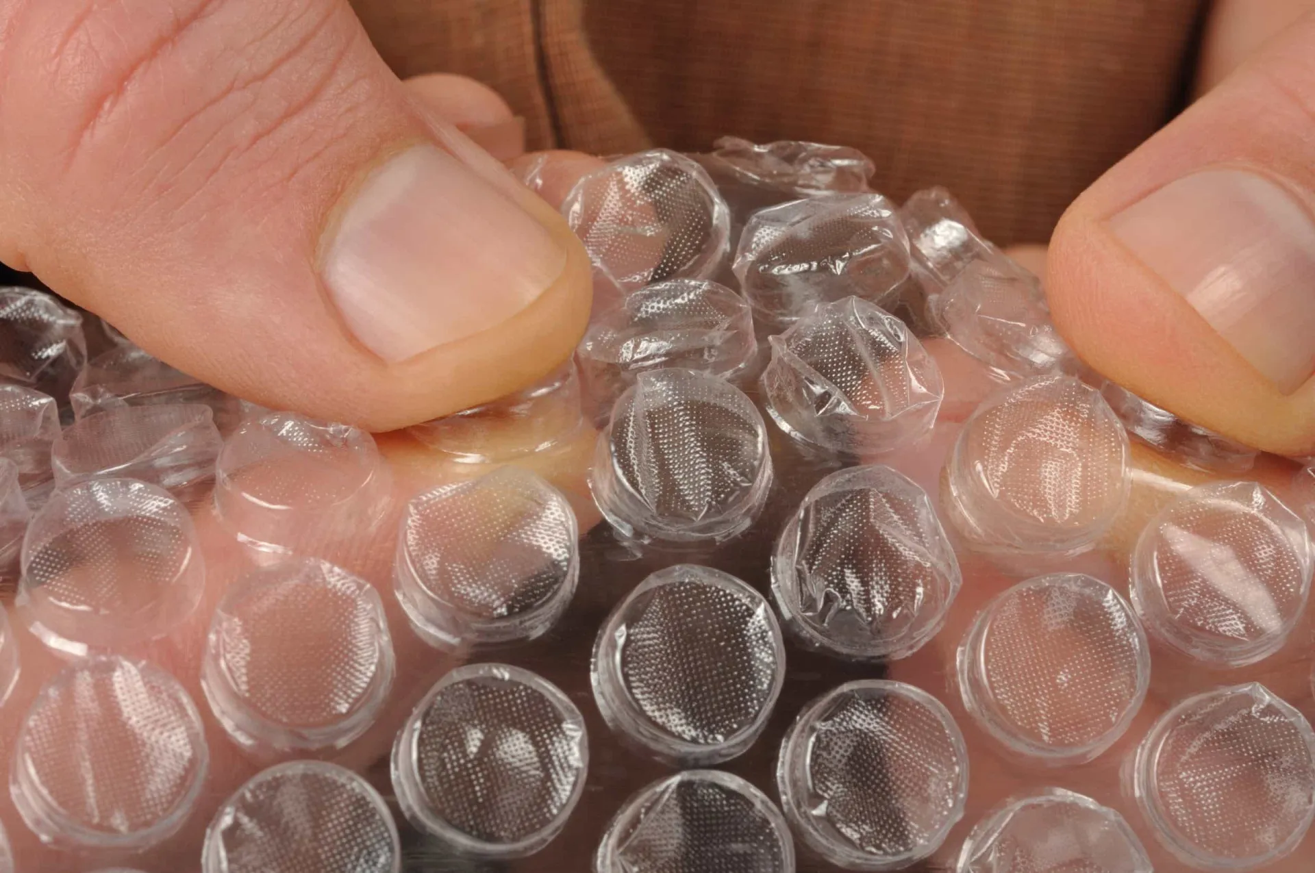 Mãos estourando as bolhas de uma folha de plástico bolha com prazer.