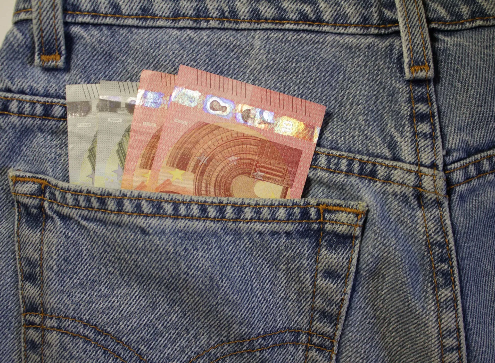 Uma mão retirando uma nota de dinheiro do bolso de uma calça jeans.