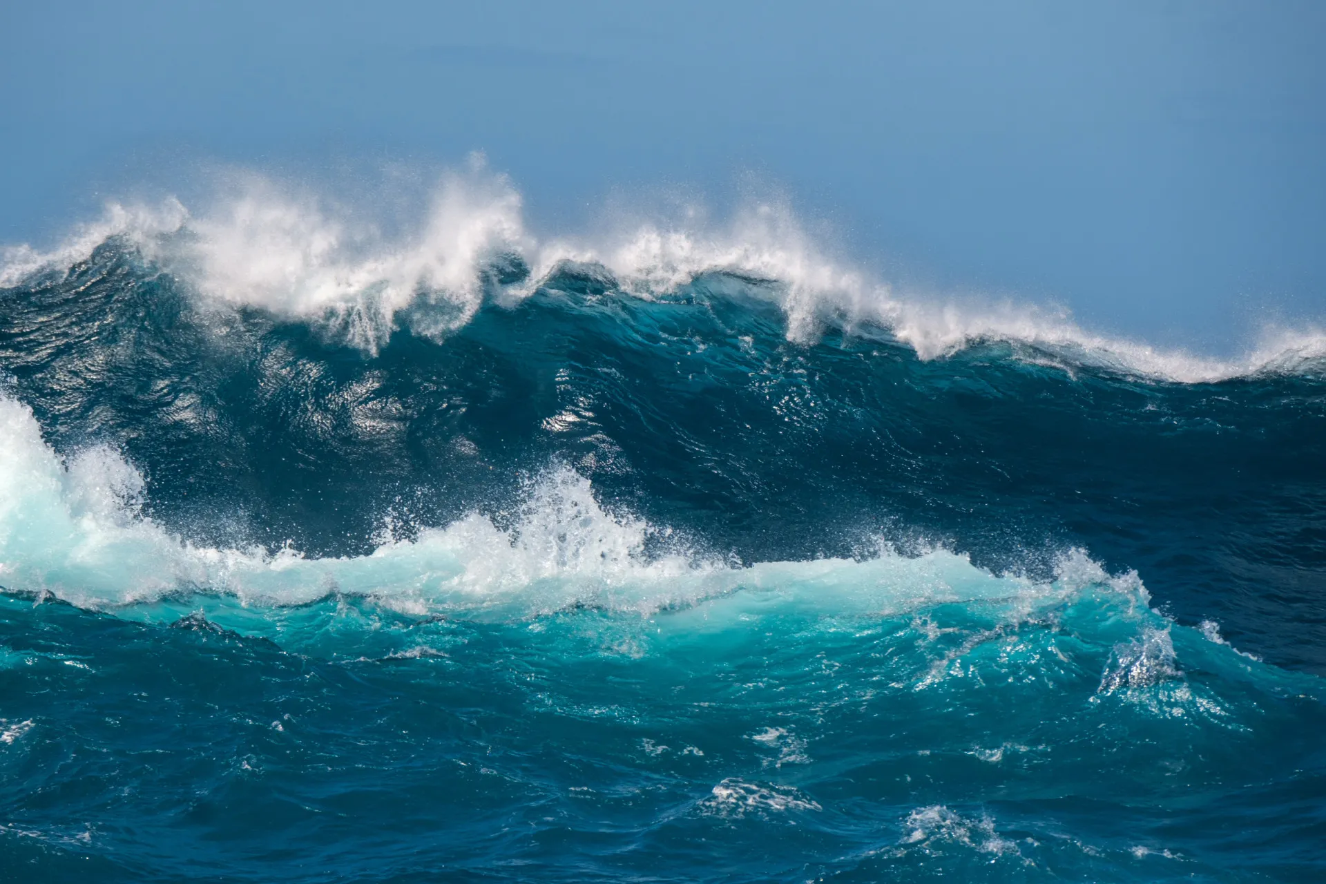 Uma onda gigante se formando no oceano, prestes a quebrar com violência.