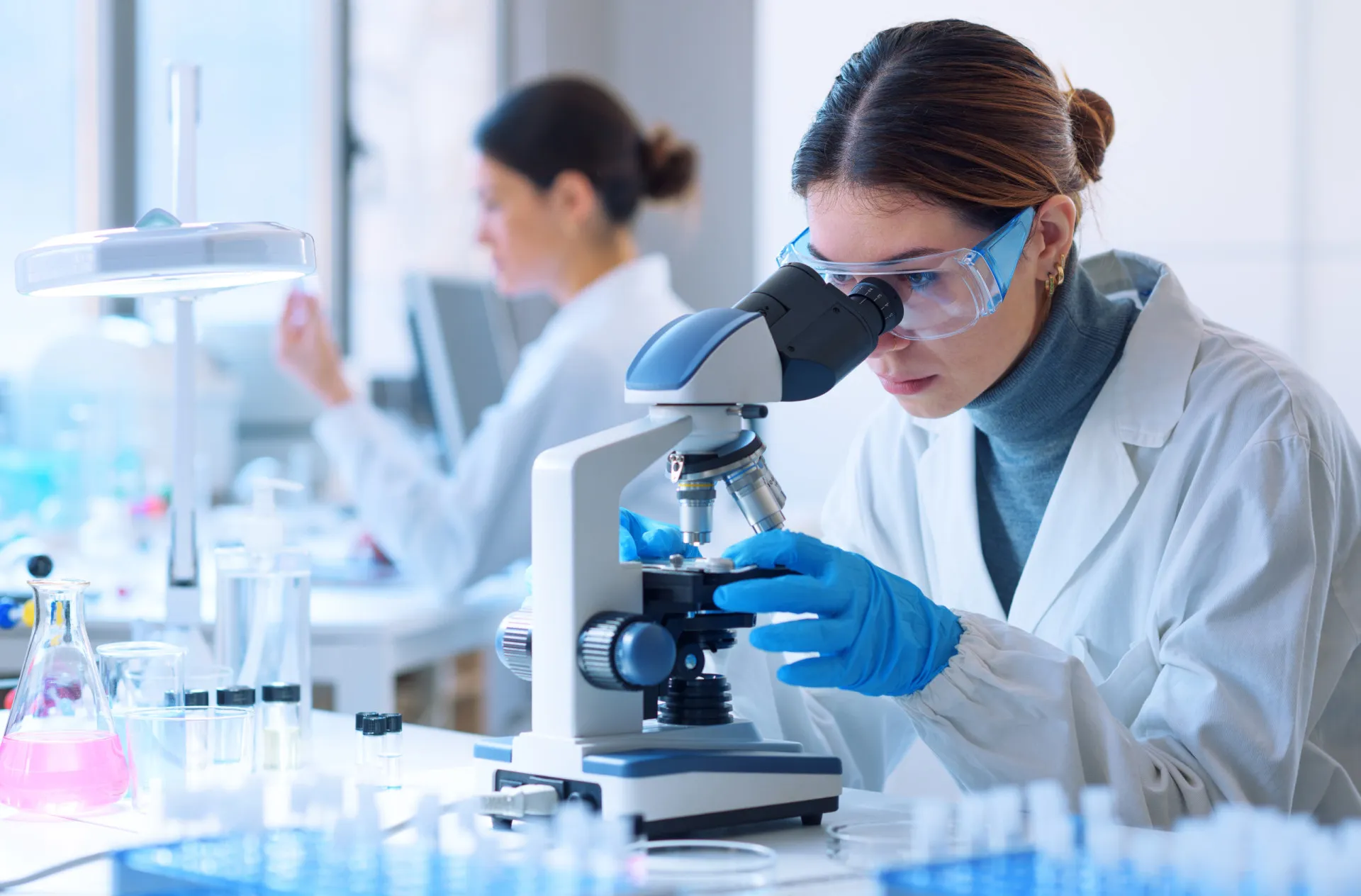 Um cientista olhando para um microscópio com uma expressão de frustração, simbolizando os desafios da pesquisa.