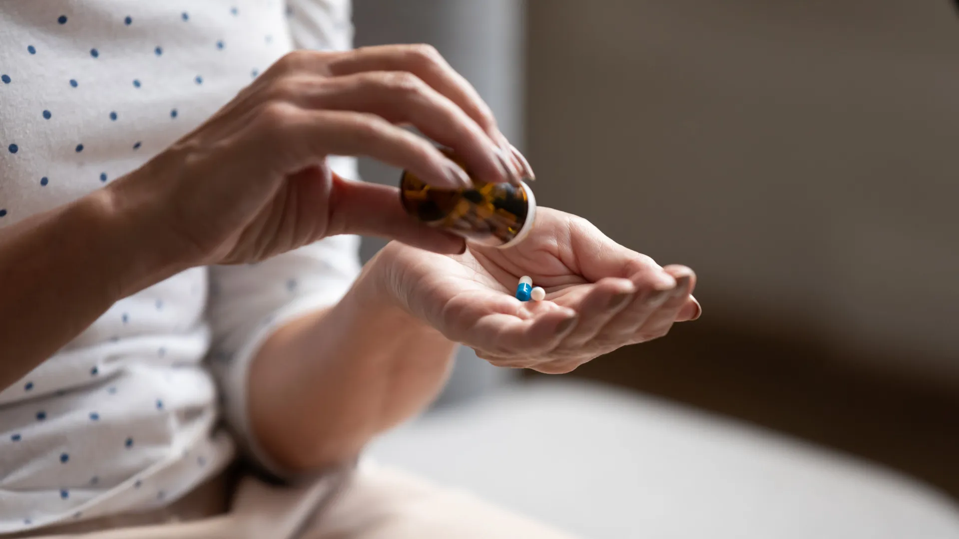 Cartelas de comprimidos de antibióticos e um copo de água sobre uma mesa.