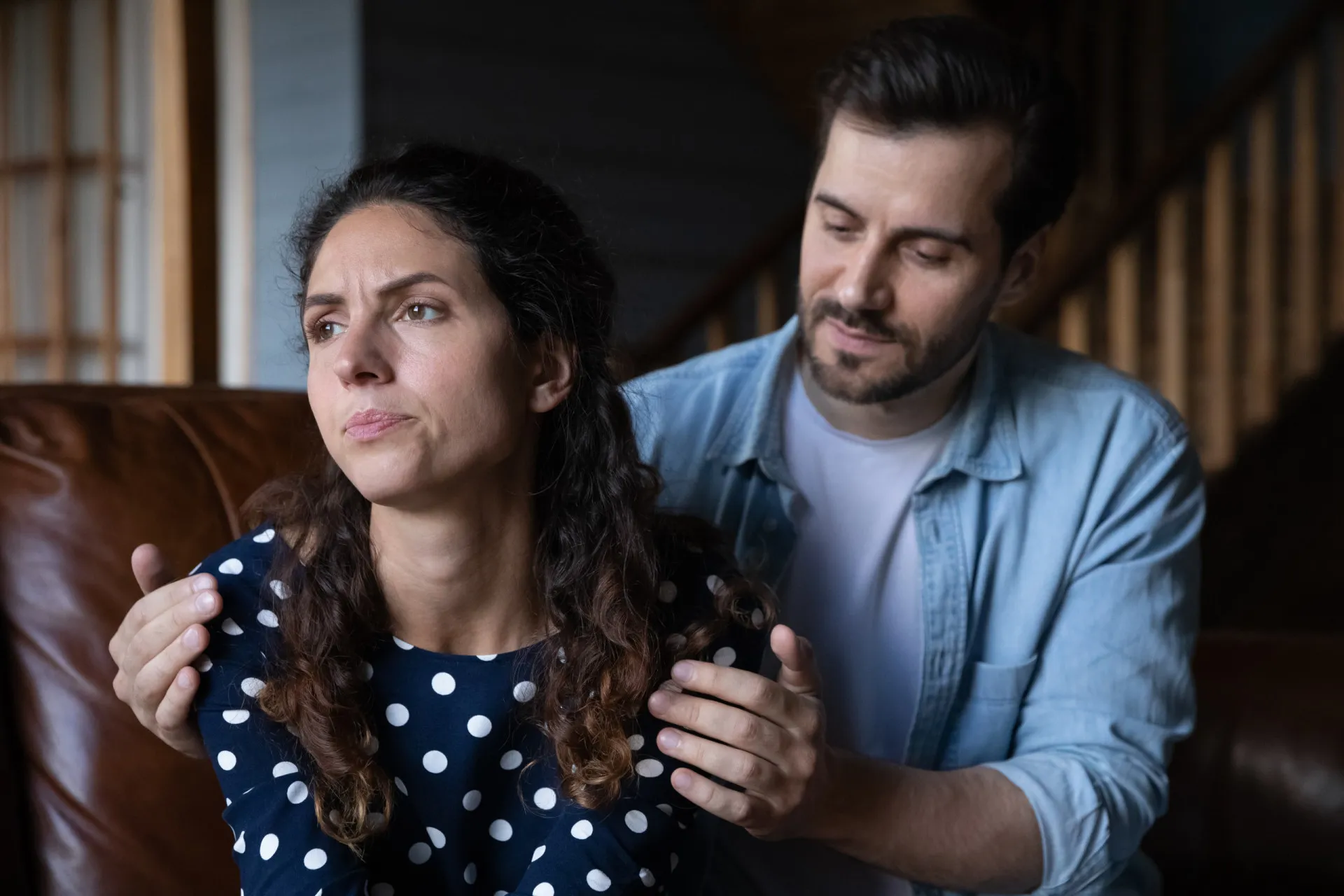 Casal sentado em um sofá, de costas um para o outro e mexendo no celular, ignorando-se mutuamente.