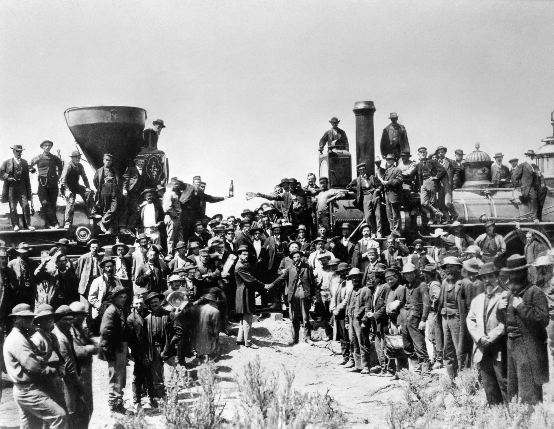Trabalhadores e engenheiros celebrando o encontro de duas locomotivas, marcando a conclusão da ferrovia transcontinental.