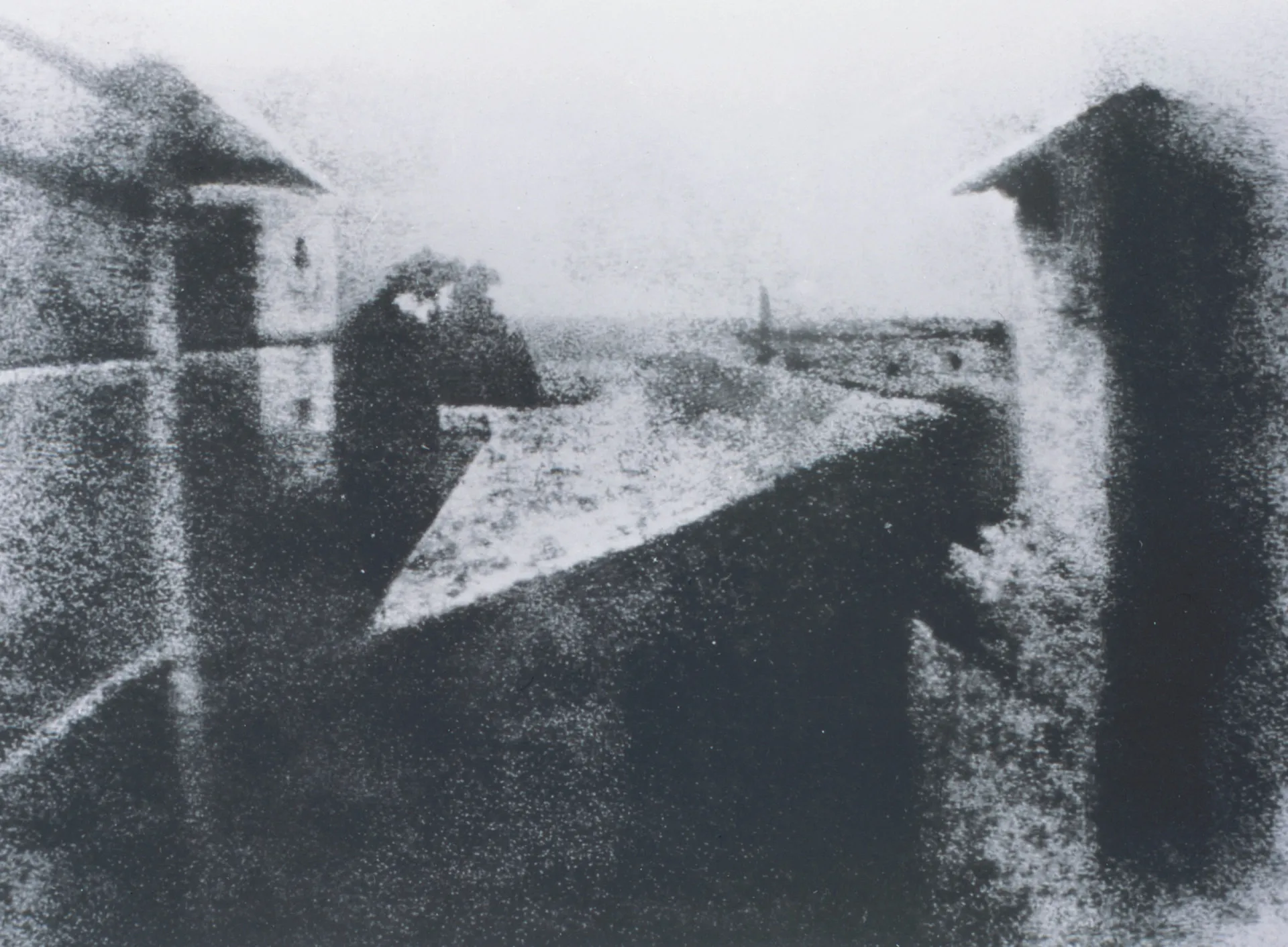 A primeira fotografia da história, uma imagem granulada e borrada de telhados vista de uma janela.